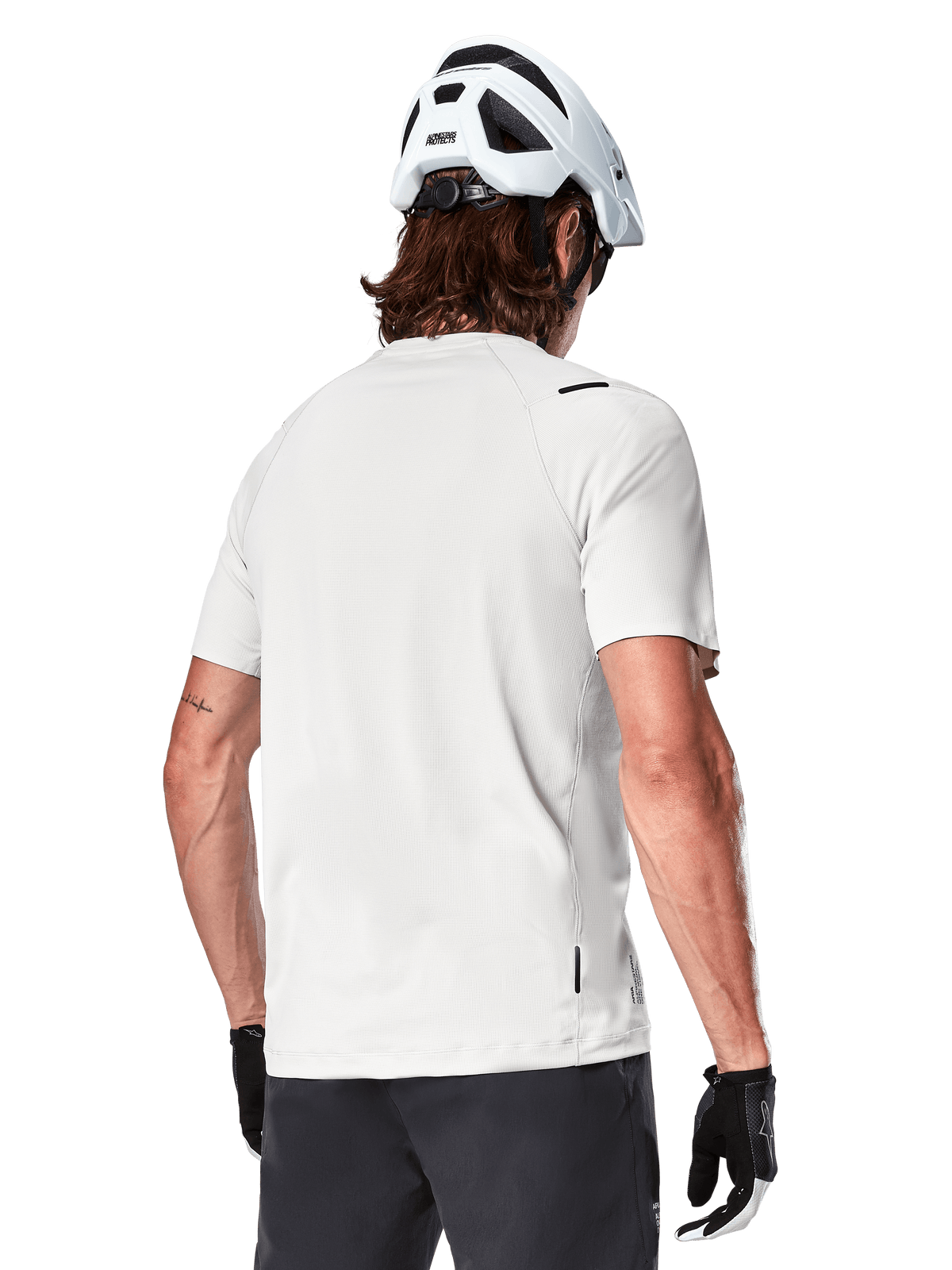 Alpinestars A-Aria Astar Jersey, Manga Curta, White Dove, vista traseira de camisola de BTT leve e respirável, usada com um capacete branco e luvas de ciclismo pretas, com cauda mais longa para maior cobertura