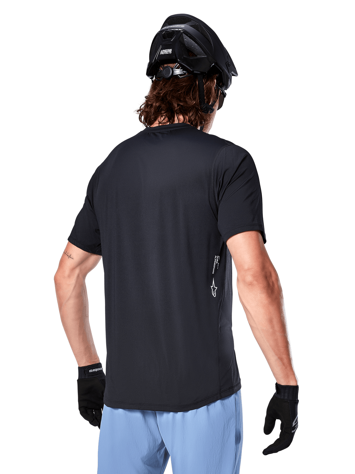Camisola Alpinestars A-Dura Oscar, camisola de ciclismo de manga curta, preta, vista traseira no ciclista, combinada com calções azul-claro e capacete de BTT preto, pequeno logótipo branco na lateral, vestuário de performance para BTT