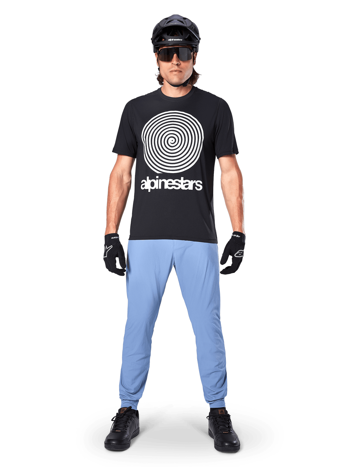 Alpinestars A-Dura Oscar Jersey - Short Sleeve, Black MTB Jersey, featuring a large white vintage Oscar spiral graphic and brand text, worn with light blue pants, black helmet, sunglasses, and black gloves, performance mountain bike apparel