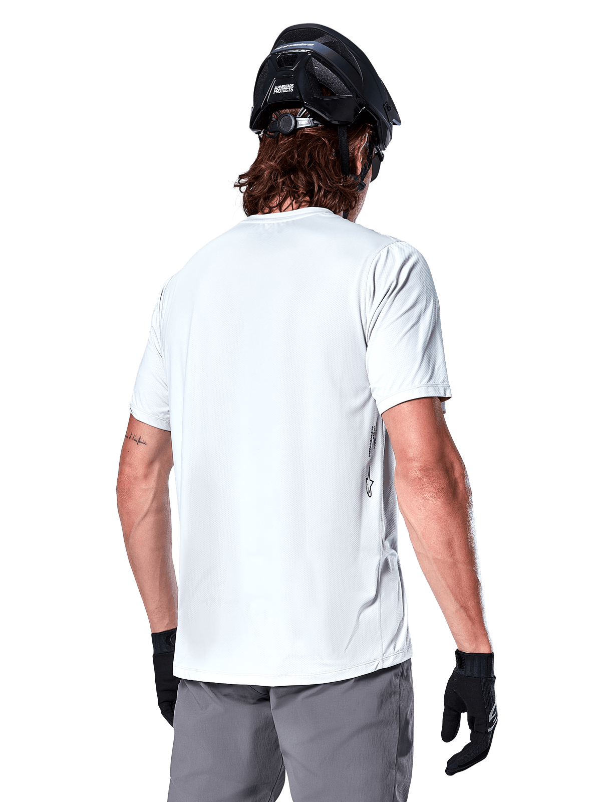 Alpinestars A-Dura Oscar Jersey, camisola de BTT de manga curta, White Dove, vista traseira de um ciclista com capacete de ciclismo preto, calções cinzentos e luvas pretas, equipamento de ciclismo de alta performance