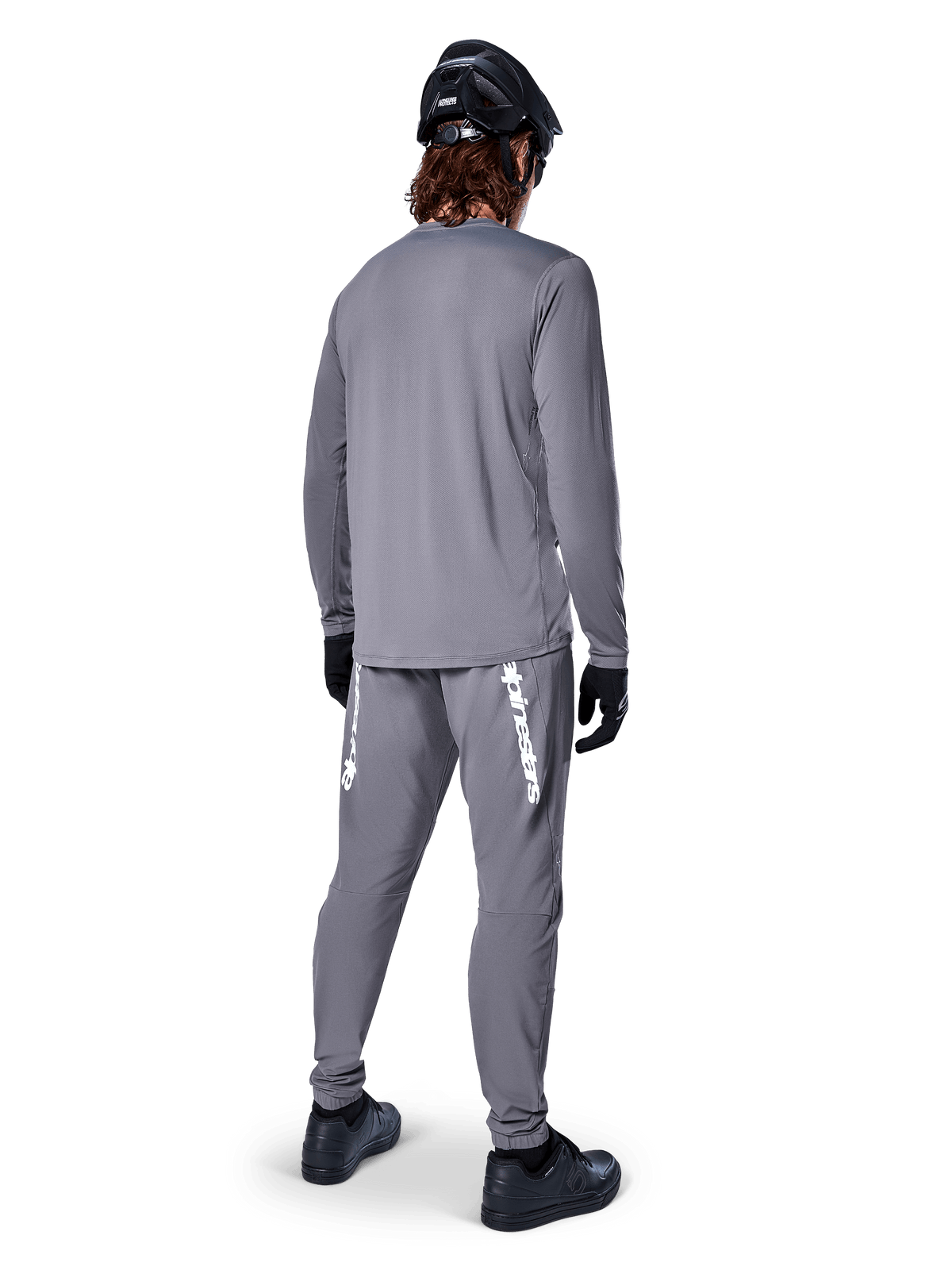 Alpinestars A-Dura Rocker Jersey de Manga Comprida, Cinza Escuro, vista traseira do modelo a usar calças de BTT cinzentas a condizer, capacete preto e luvas pretas, design de vestuário profissional para bicicleta de montanha