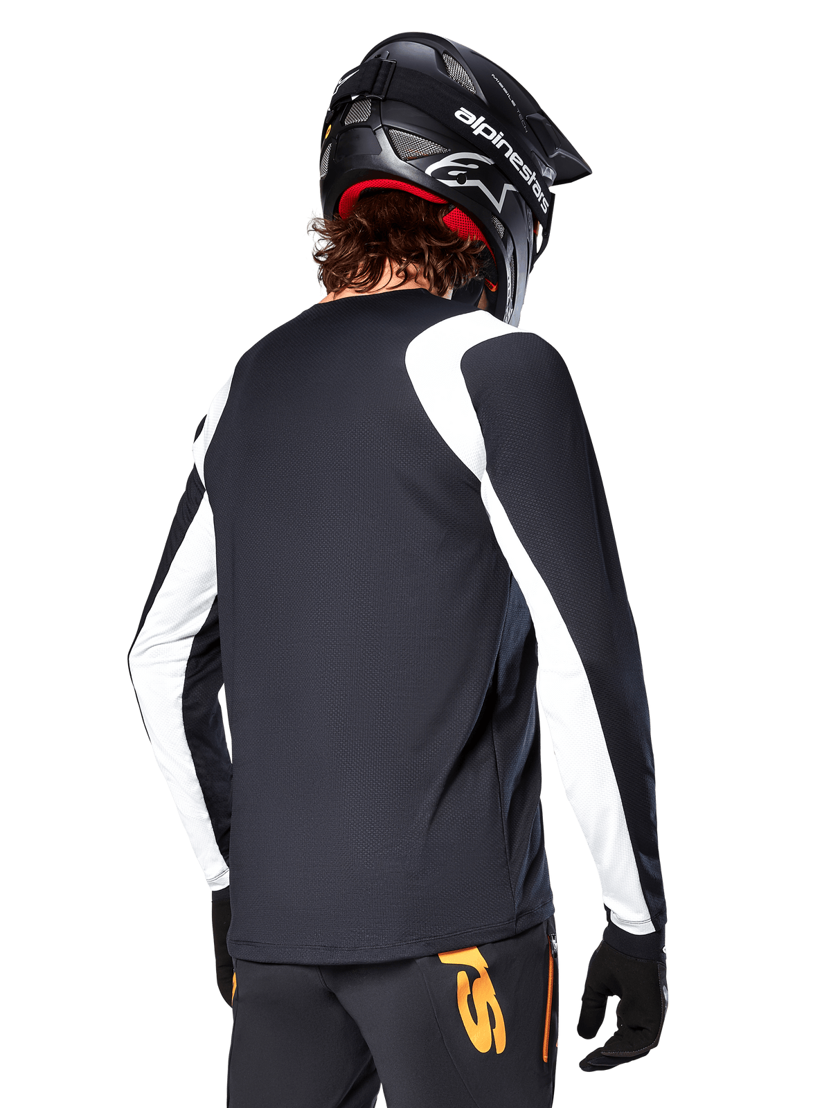 Ciclista de BTT a usar a Camisola de Manga Longa Alpinestars A-Supra Oscar, preta com painéis brancos nos ombros e mangas, vista de costas, capacete e luvas pretas, calças com detalhes laranja, equipamento de ciclismo de montanha durável
