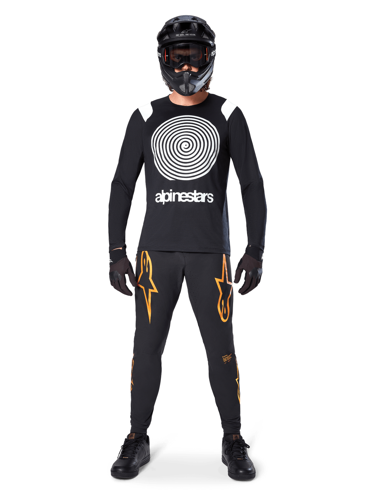 Modelo masculino com equipamento completo de mountain bike, Camisola de Manga Comprida Alpinestars A-Supra Oscar em preto com gráfico espiral branco no peito, calças pretas com logótipos de estrela cor de laranja, capacete integral e óculos pretos, luvas e sapatos pretos, conjunto coordenado para a prática de MTB gravity