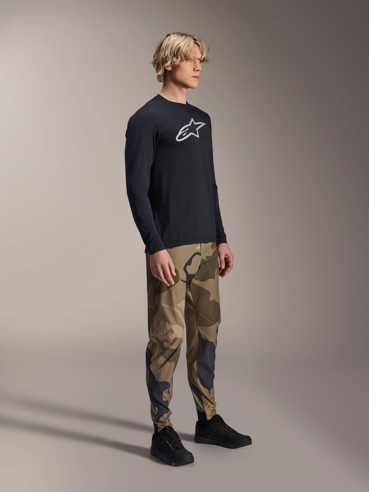 Alpinestars A-Dura Camo Pant, calças de BTT, camuflagem castanha, usadas com uma camisola de manga comprida A-Dura Astar preta e sapatos pretos, vestuário técnico de BTT para trail riding.