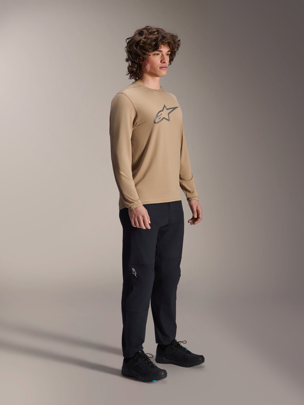 Camisola de Manga Comprida Alpinestars A-Dura Astar, castanho claro, vestida por um modelo com calças e sapatos pretos, com logótipo Astars cinzento no peito, equipamento de performance casual para bicicleta de montanha