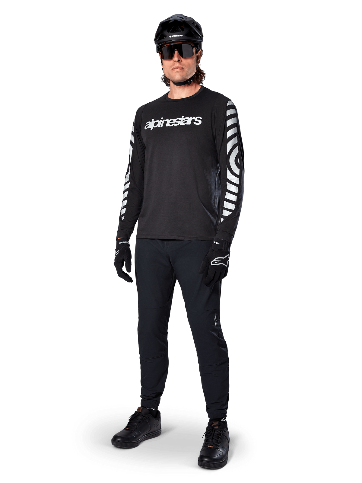 Alpinestars A-Dura Dri Oscar Long Sleeve Jersey, camisola de manga comprida, preto refletor, com logótipo Alpinestars branco no peito e padrões gráficos refletores nas mangas, usada com calças de BTT pretas, capacete e luvas, vestuário técnico de BTT