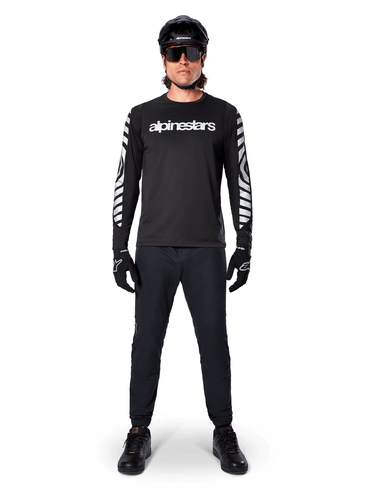Alpinestars A-Dura Dri Oscar Long Sleeve Jersey em Black Reflective, usada com um capacete preto e óculos de sol, com logótipo branco no peito e padrões gráficos refletivos nas mangas, equipamento de MTB para percursos fora de estrada
