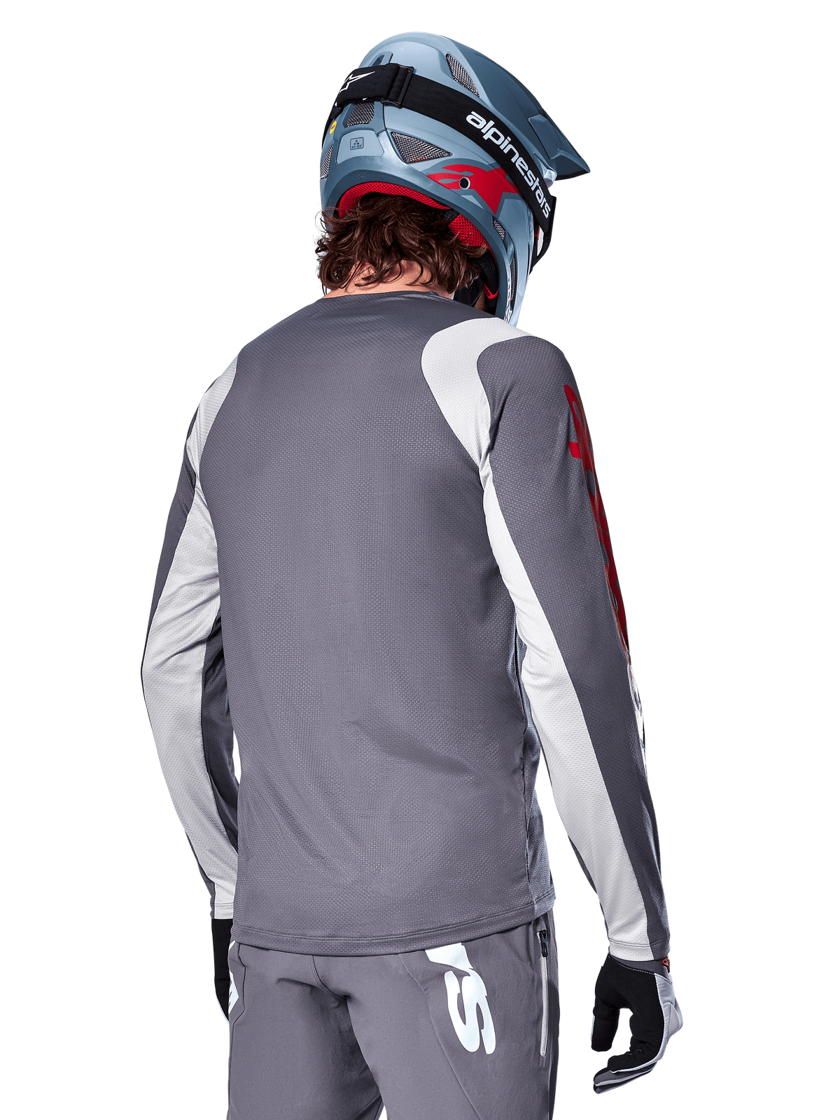 Camisola de Manga Comprida Alpinestars A-Supra Astar, cinzento escuro com painéis cinzento claro nos ombros e braços, vista traseira de ciclista com capacete integral de mountain bike azul e calças cinzentas, vestuário de ciclismo MTB de ajuste de performance