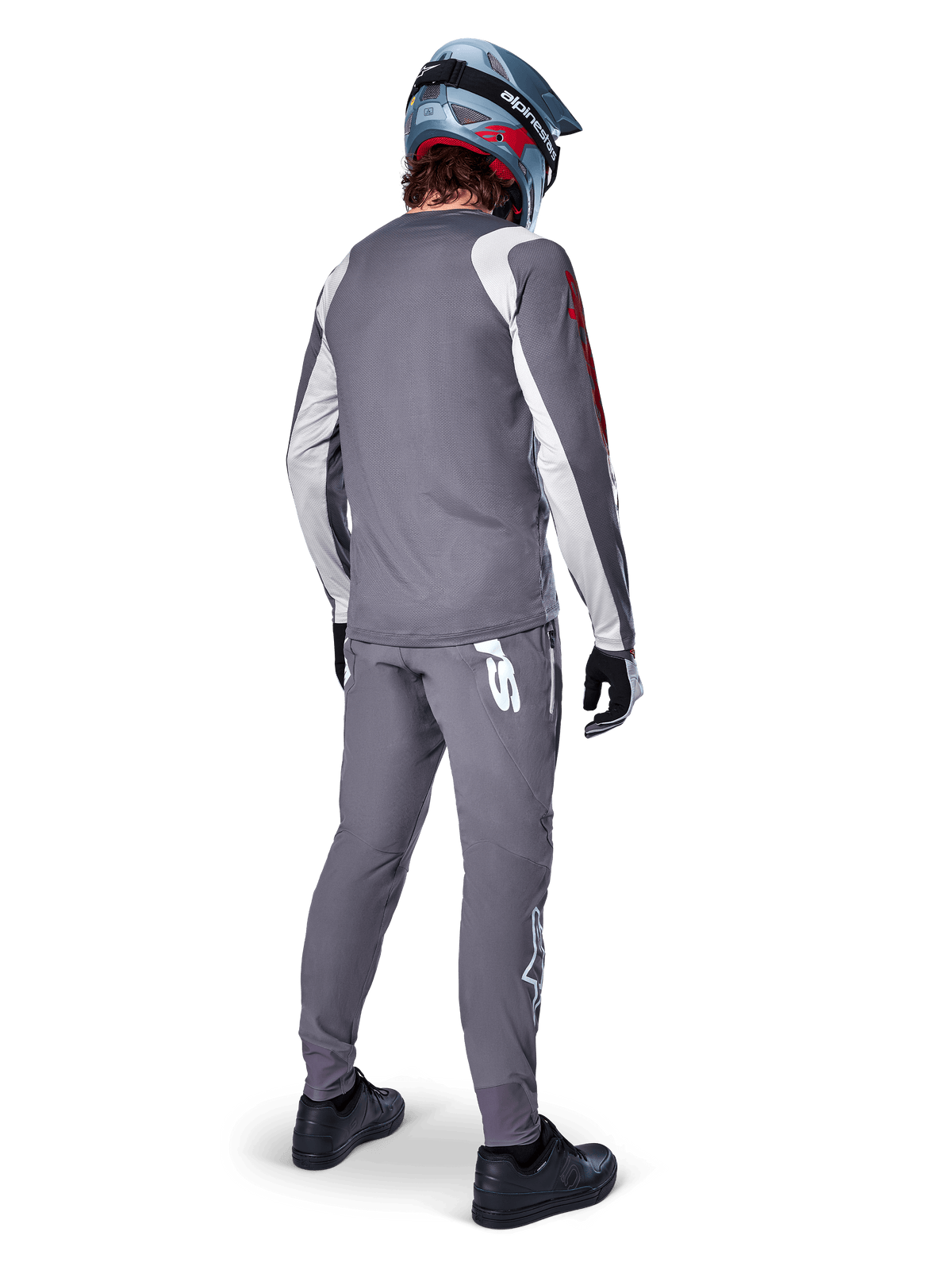 Camisola Alpinestars A-Supra Astar, camisola de BTT de manga comprida, cinzento escuro com detalhes brancos nas mangas e logótipo vermelho, vista traseira de ciclista a usar calças cinzentas a condizer e capacete integral azul, vestuário de ciclismo de performance