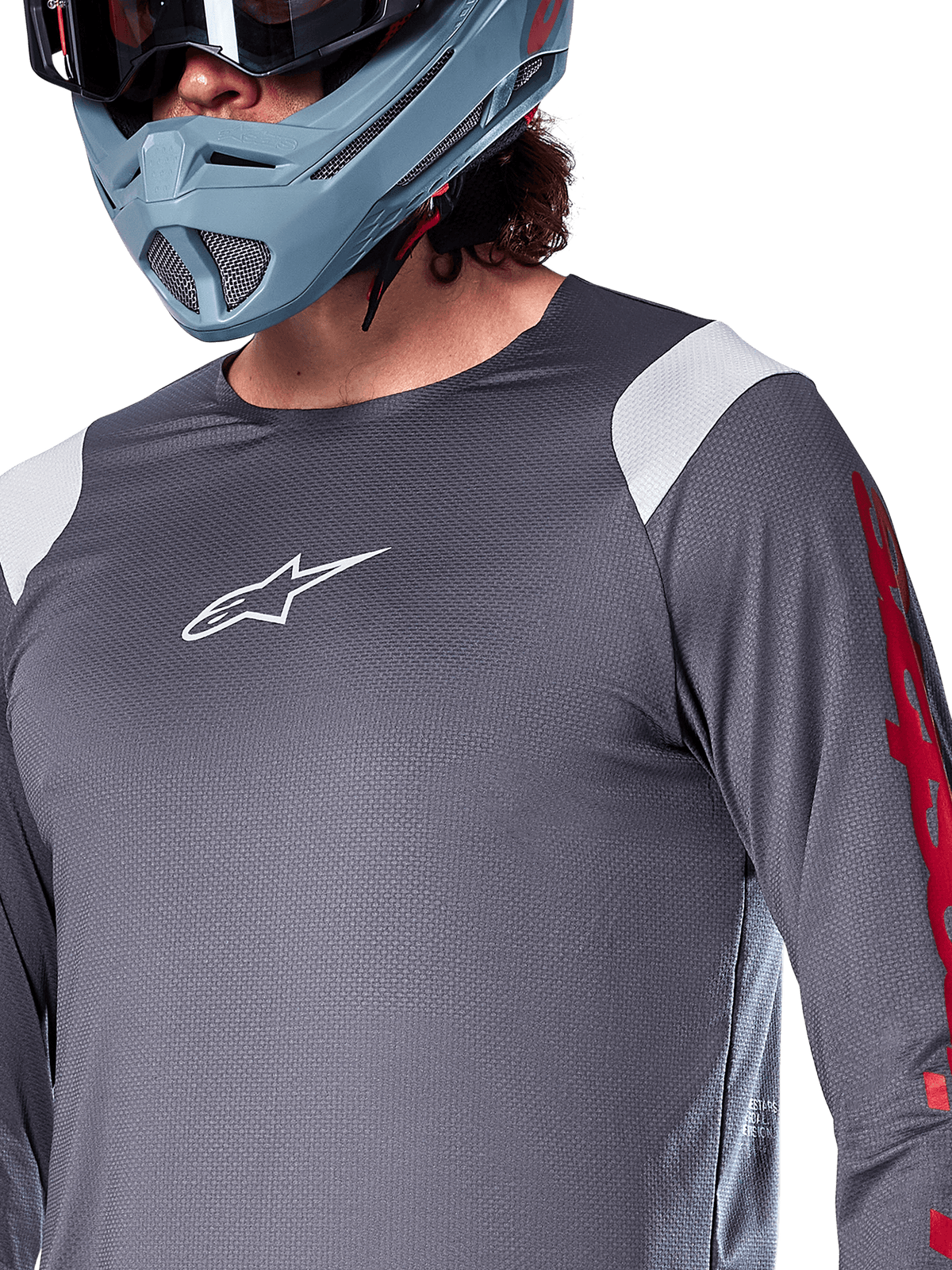 Camisola de Manga Comprida Alpinestars A-Supra Astar, cinza escuro com painéis brancos nos ombros e grafismos vermelhos na manga, usada com um capacete integral cinza-azulado claro, vestuário de BTT de alta performance