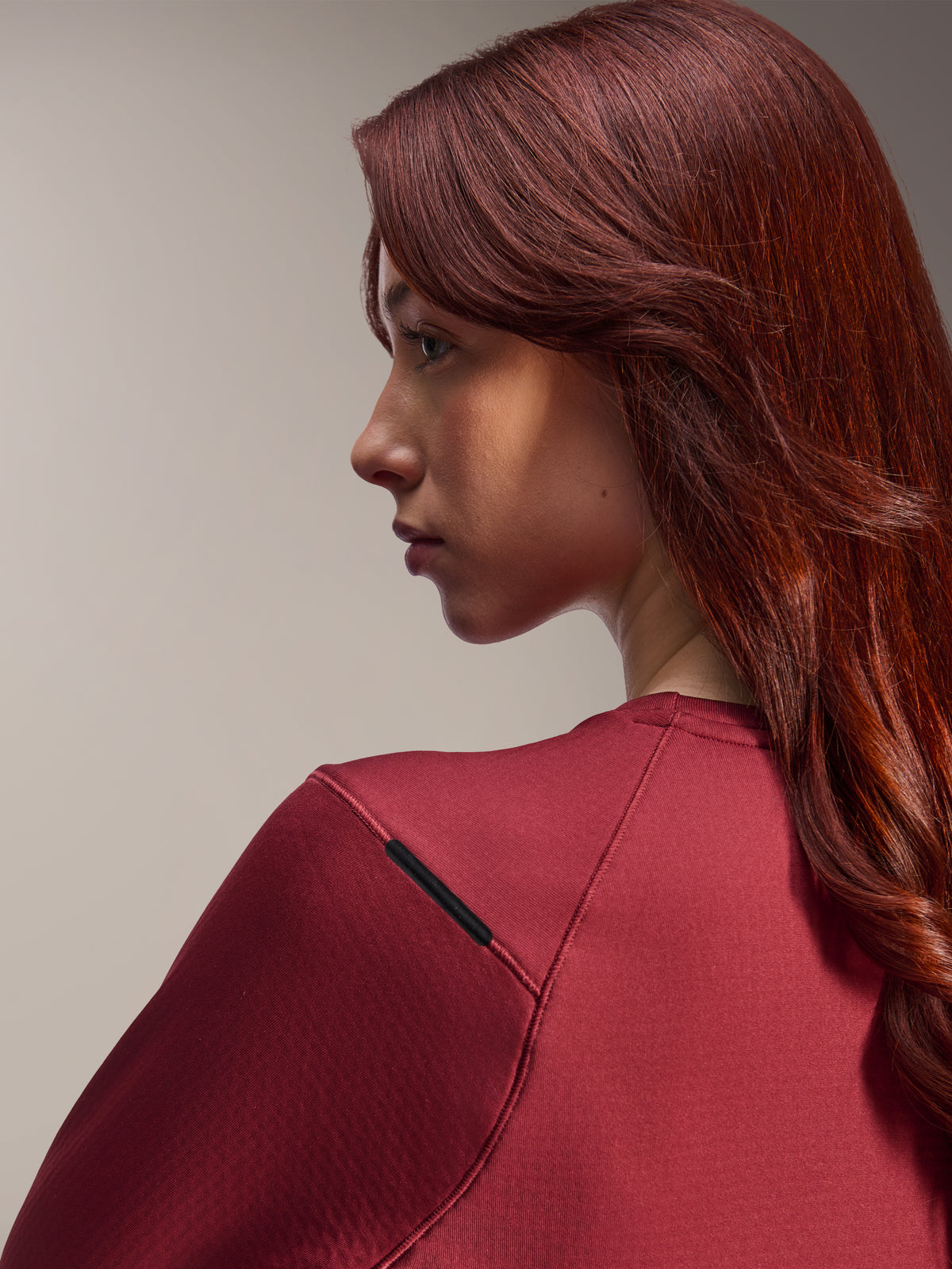 Mulher a usar camisola térmica Alpinestars Stella A-Dura, camisola de BTT de manga comprida bordeaux, vista de perfil lateral em grande plano, foco no detalhe da costura do ombro e na textura do material, equipamento de ciclismo lifestyle