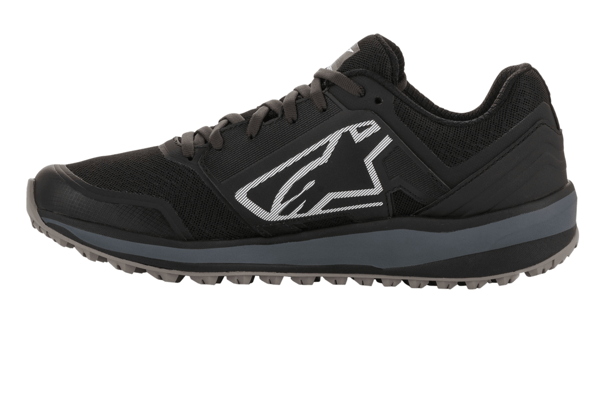 Sapatos Alpinestars Meta Trail, sapatos de corrida de alta performance, pretos e cinzento escuro, perfil lateral com grande logótipo Astars branco, entressola cinzento escuro, sola de borracha com relevos resistente ao óleo, concebidos para conforto no paddock e utilização por equipas de desportos motorizados