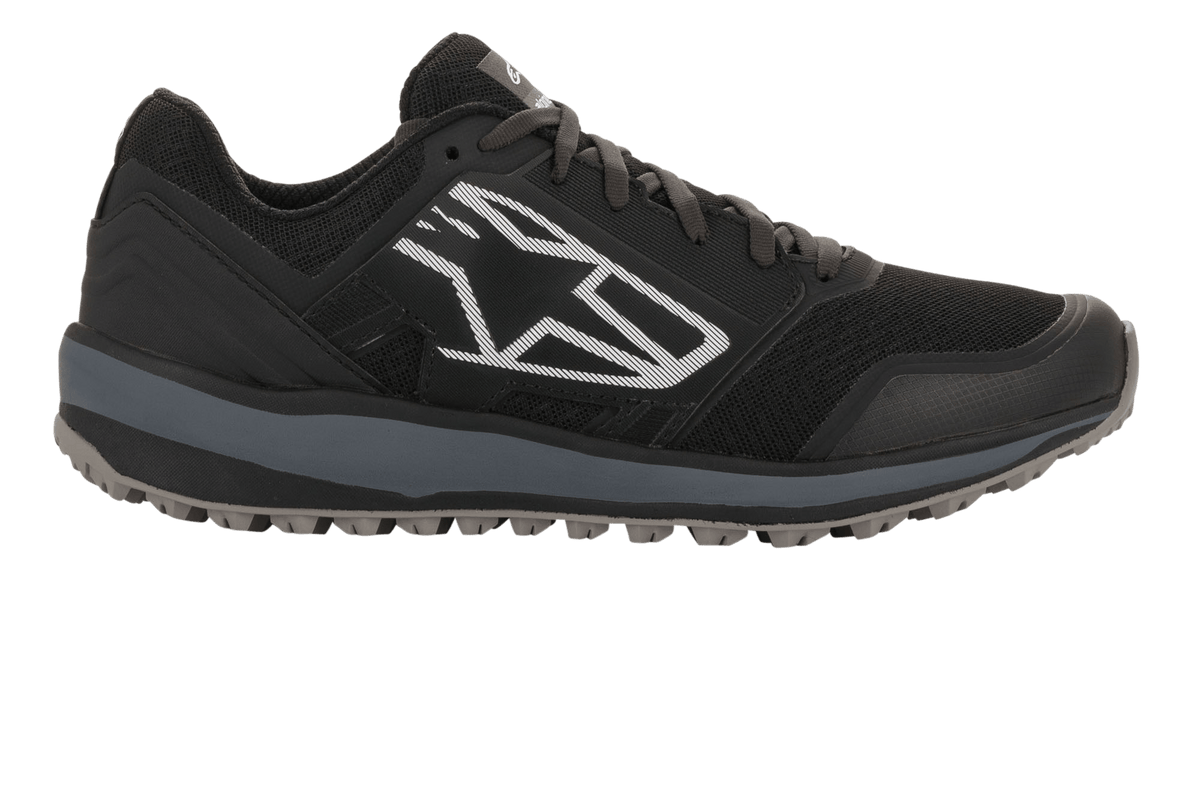 Sapatos Alpinestars Meta Trail, sapatos de corrida de performance, pretos e cinzento escuro, perfil lateral com um grande logótipo Astars geométrico branco, parte superior em malha, entressola cinzenta e sola de borracha com relevos, calçado casual de paddock para desportos motorizados