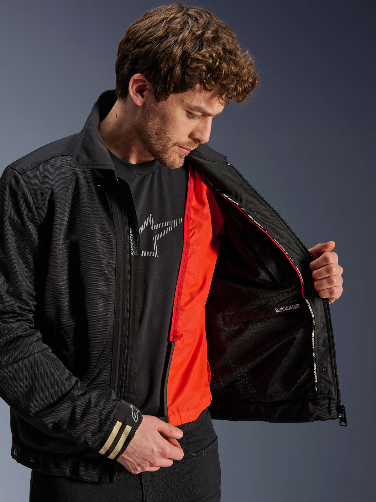 Casaco Alpinestars Ignite Air, casaco de motociclismo urbano preto, com forro corta-vento destacável em laranja vibrante e corpo em malha, vista interior mostrando compartimento impermeável, usado com t-shirt preta com logótipo Alpinestars