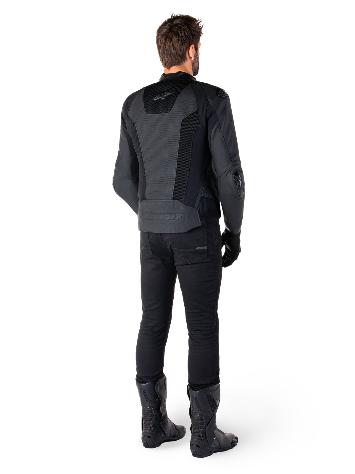 Vista traseira de um homem a usar o casaco de couro Alpinestars Missile V3 Airflow em preto, com painéis perfurados extensos para ventilação, combinado com calças e botas de motociclismo pretas, exibindo uma estética de corrida aerodinâmica.