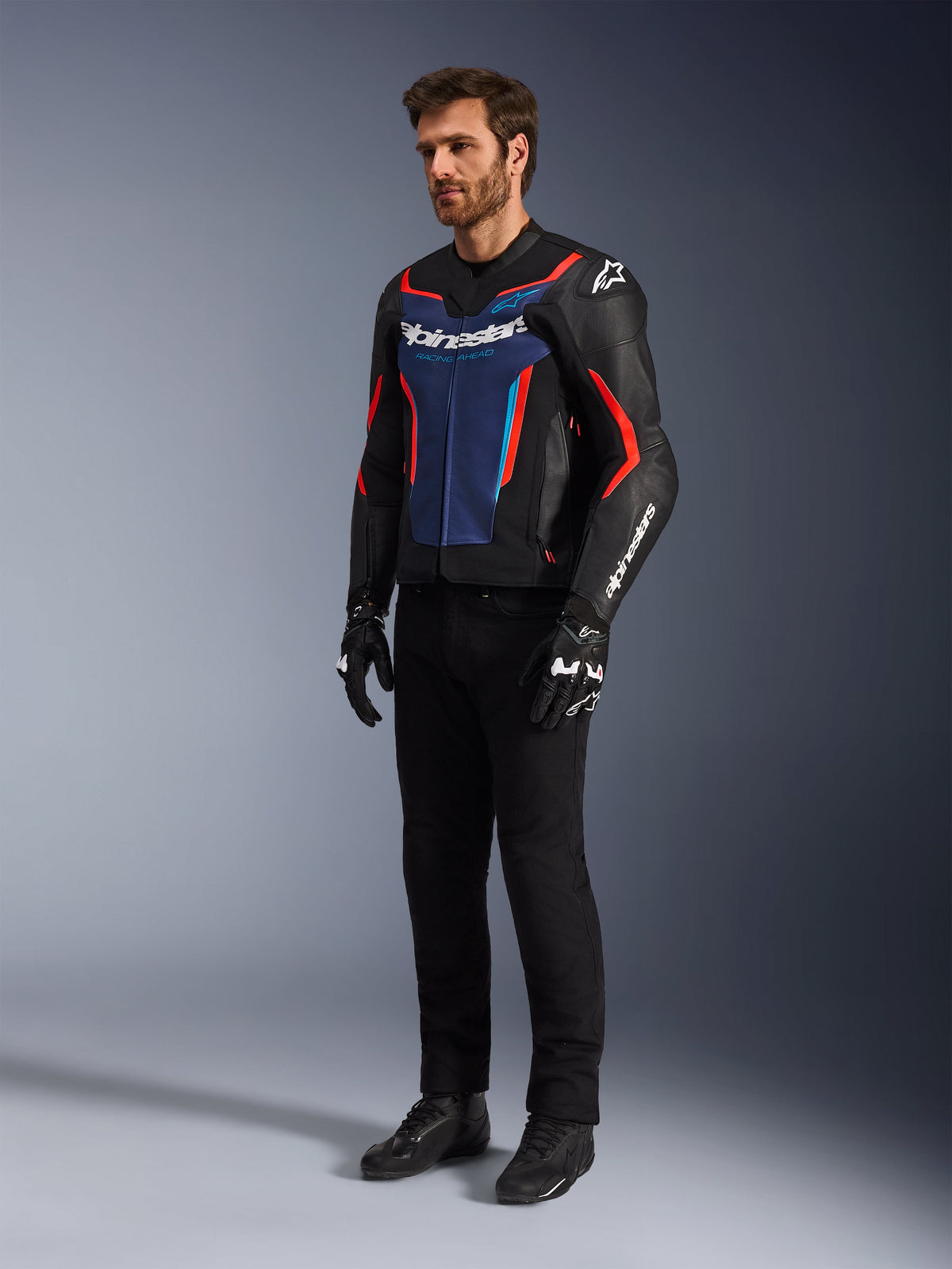 Modelo a usar o Casaco de Pele Alpinestars GP Force V2 em Preto Azul Vermelho Fluo, combinado com calças de condução técnicas pretas, luvas pretas e botas, equipamento profissional de motociclismo para condução desportiva