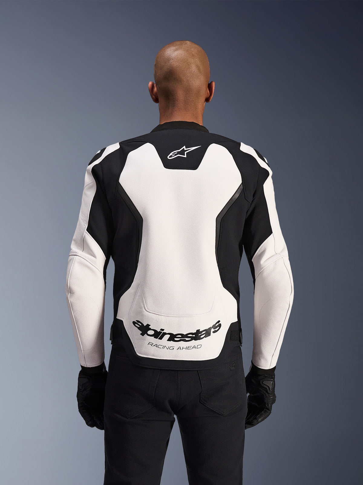 Alpinestars GP Force V2 Leather Jacket, White and Black, back view on a model, featuring a white leather panel with black side accents, Alpinestars logo at the nape and 'RACING AHEAD' branding on the lower back, sport motorcycle racing jacket