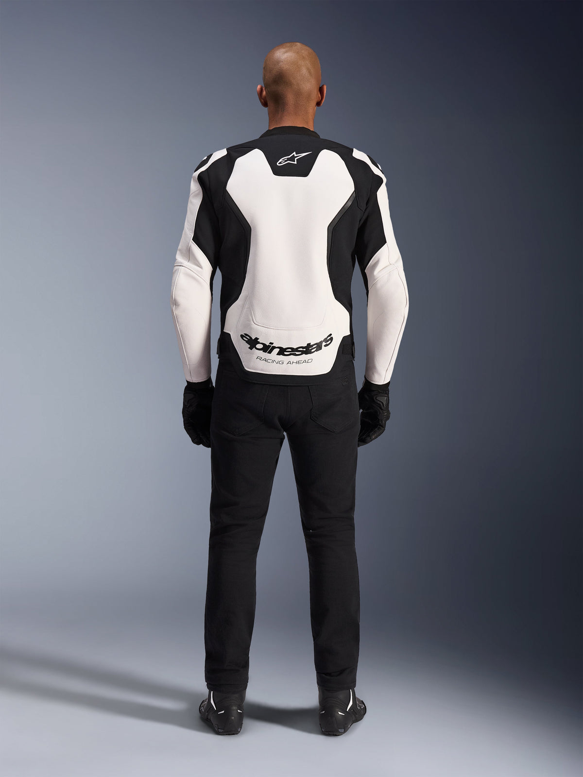Alpinestars GP Force V2 Leather Jacket, White and Black, rear view showing large white back panel with Alpinestars logo and 'RACING AHEAD' text, worn with black riding pants and gloves, sport motorcycle gear design