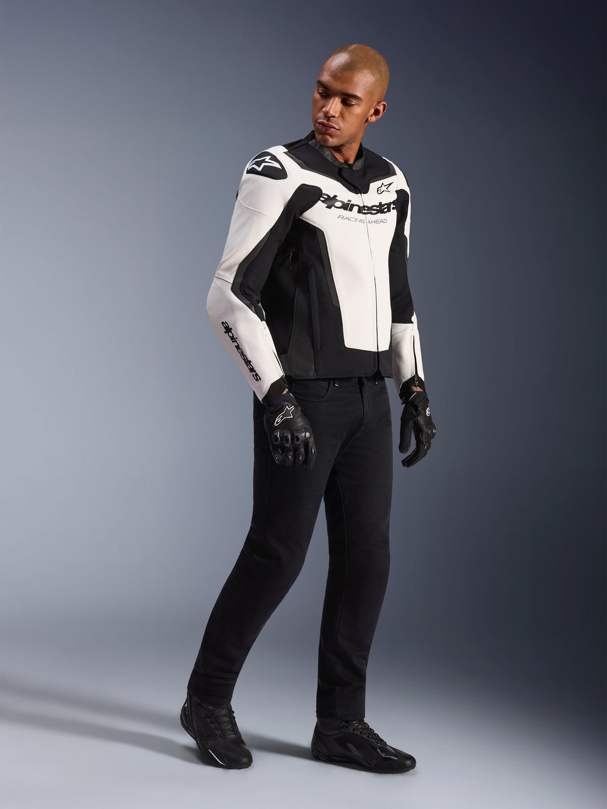 Male model wearing Alpinestars GP Force V2 Leather Jacket, White and Black, styled with black motorcycle pants and gloves, sport-oriented bovine leather design with bold branding, full-body studio shot