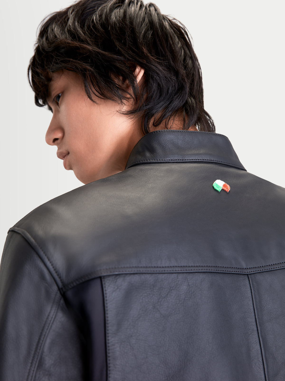 Alpinestars Maver X Casaco de couro, blusão de moto urbano para homem em preto, vista traseira em primeiro plano a mostrar construção em couro bovino premium, gola de motociclista e detalhe da bandeira italiana num modelo