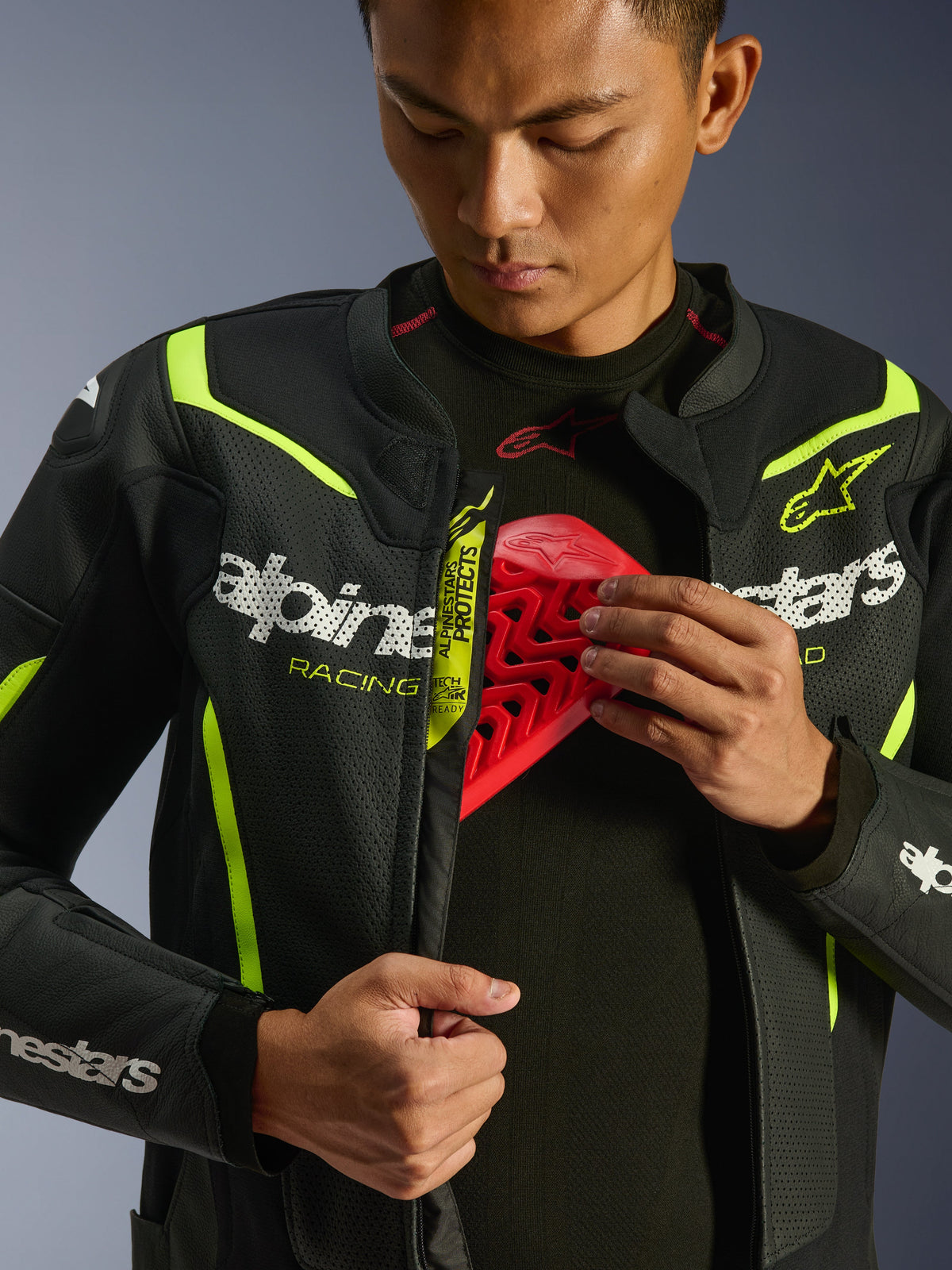 Alpinestars GP Force V2 Air Leather Jacket, preto e amarelo fluo, casaco de motociclismo em couro perfurado, vestido por um piloto a demonstrar o compartimento peitoral com uma inserção de protetor vermelha, com logótipo Alpinestars branco e perfurações de fluxo de ar extensas