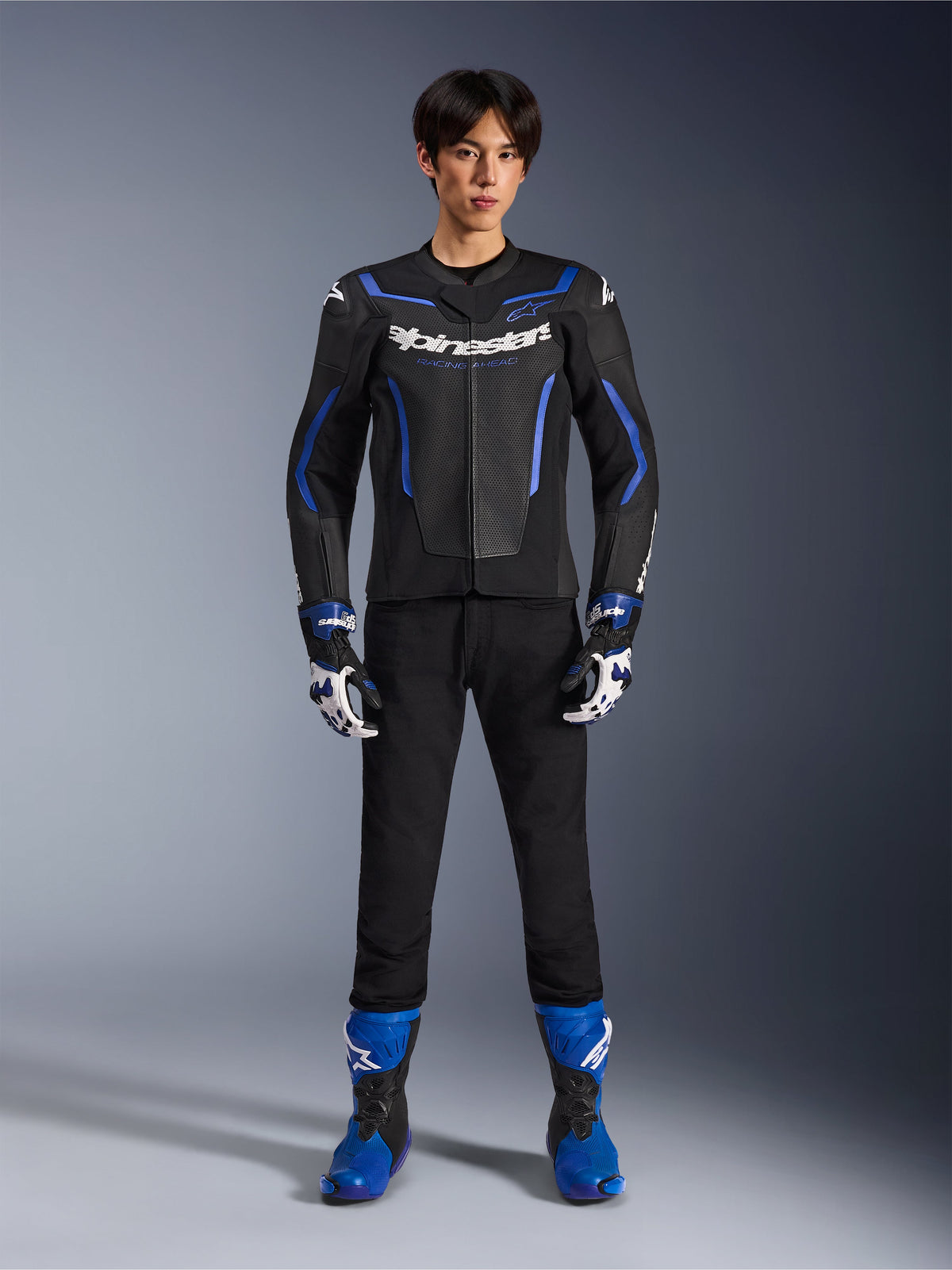 Alpinestars GP Force V2 Airflow Leather Jacket em Black Metallic Blue, usado com luvas de corrida a condizer, calças pretas e botas azuis, equipamento profissional de motociclismo desportivo, fotografia de estúdio de corpo inteiro