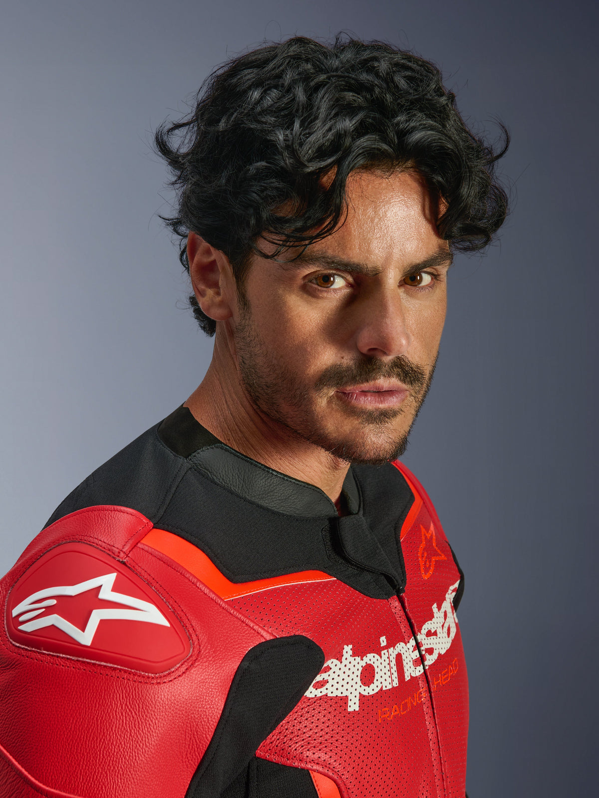 Alpinestars GP Force V2 Air Leather Jacket, Red and Red Fluo, worn by a man in a close-up portrait, featuring perforated bovine leather, white Alpinestars branding on the chest and shoulder, and black textile accents, professional motorcycle racing gear