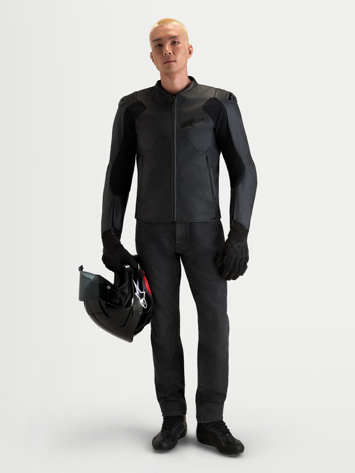 Casaco de moto Alpinestars Caliber V 2, blusão em couro preto para homem com proteção com classificação AA, ombros DFS de perfil baixo e construção em couro de bovino de flor inteira, vestido por um modelo a segurar um capacete preto