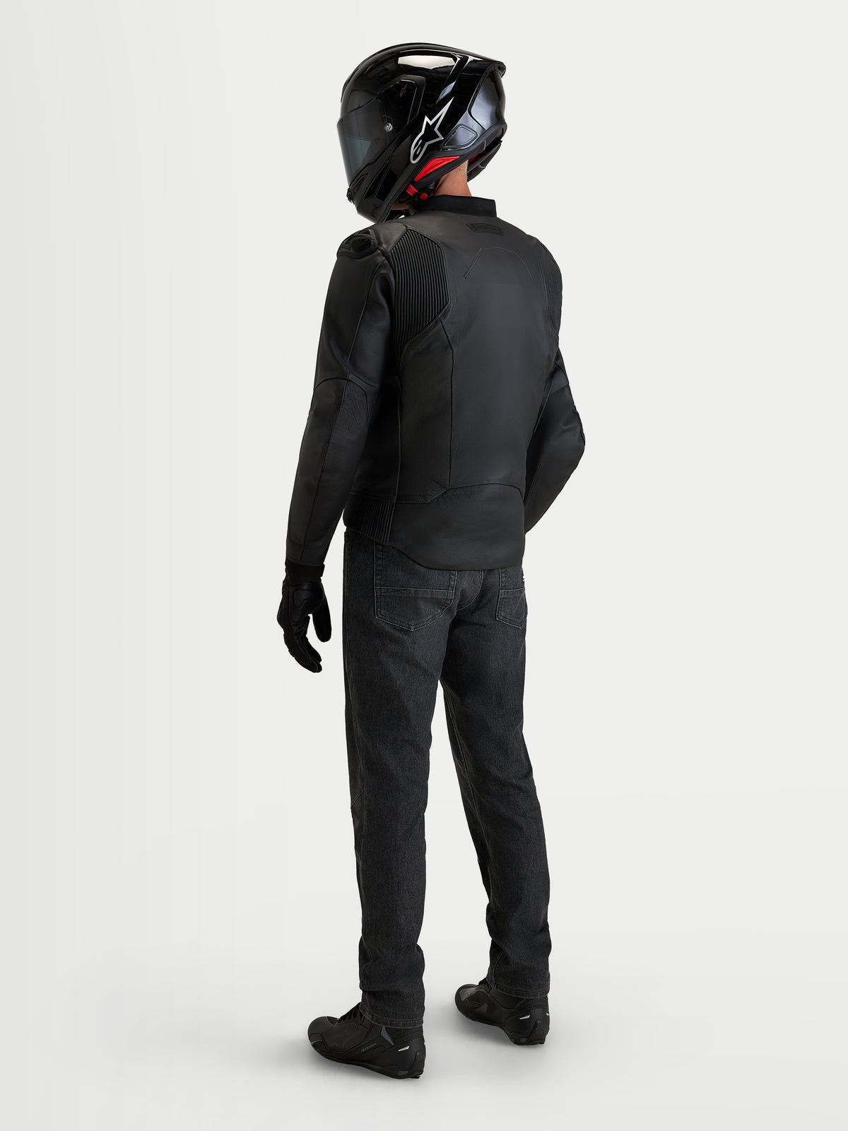 Alpinestars Caliber V 2 blusão de pele, blusão de moto desportivo para homem em couro preto, vista traseira de um condutor com equipamento completo, capacete e calças de ganga pretas