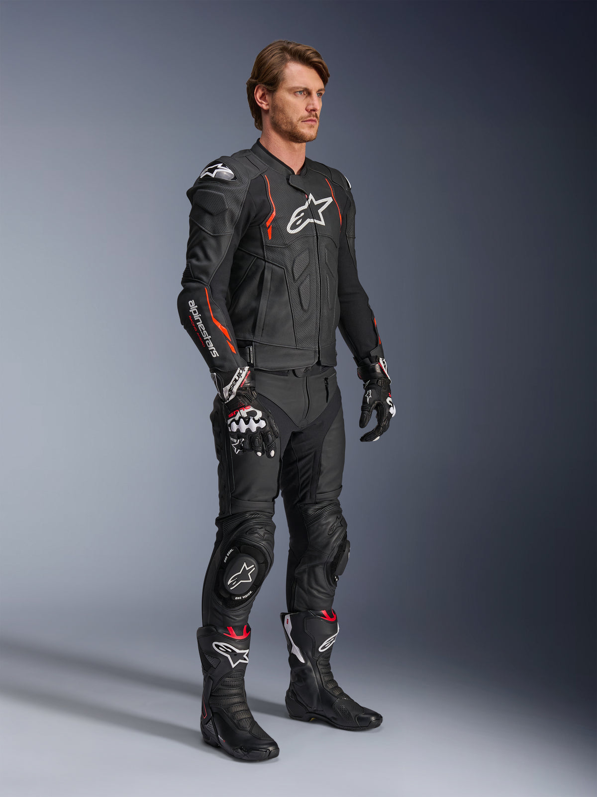 Casaco de Couro Alpinestars Dusk Airflow, Preto Vermelho Fluo, usado como parte de um equipamento de motociclismo completo com calças de couro, luvas e botas a condizer, apresentando construção em couro perfurado e detalhes desportivos.