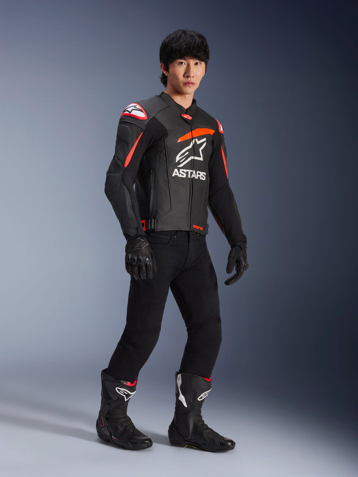 Piloto a usar Jaqueta de Couro Alpinestars GP Plus R V4 Airflow, preta com detalhes em vermelho fluo e branco, com couro perfurado e logótipo ASTARS no peito, acompanhada por calças de condução pretas e botas de motociclista pretas, equipamento de performance desportiva
