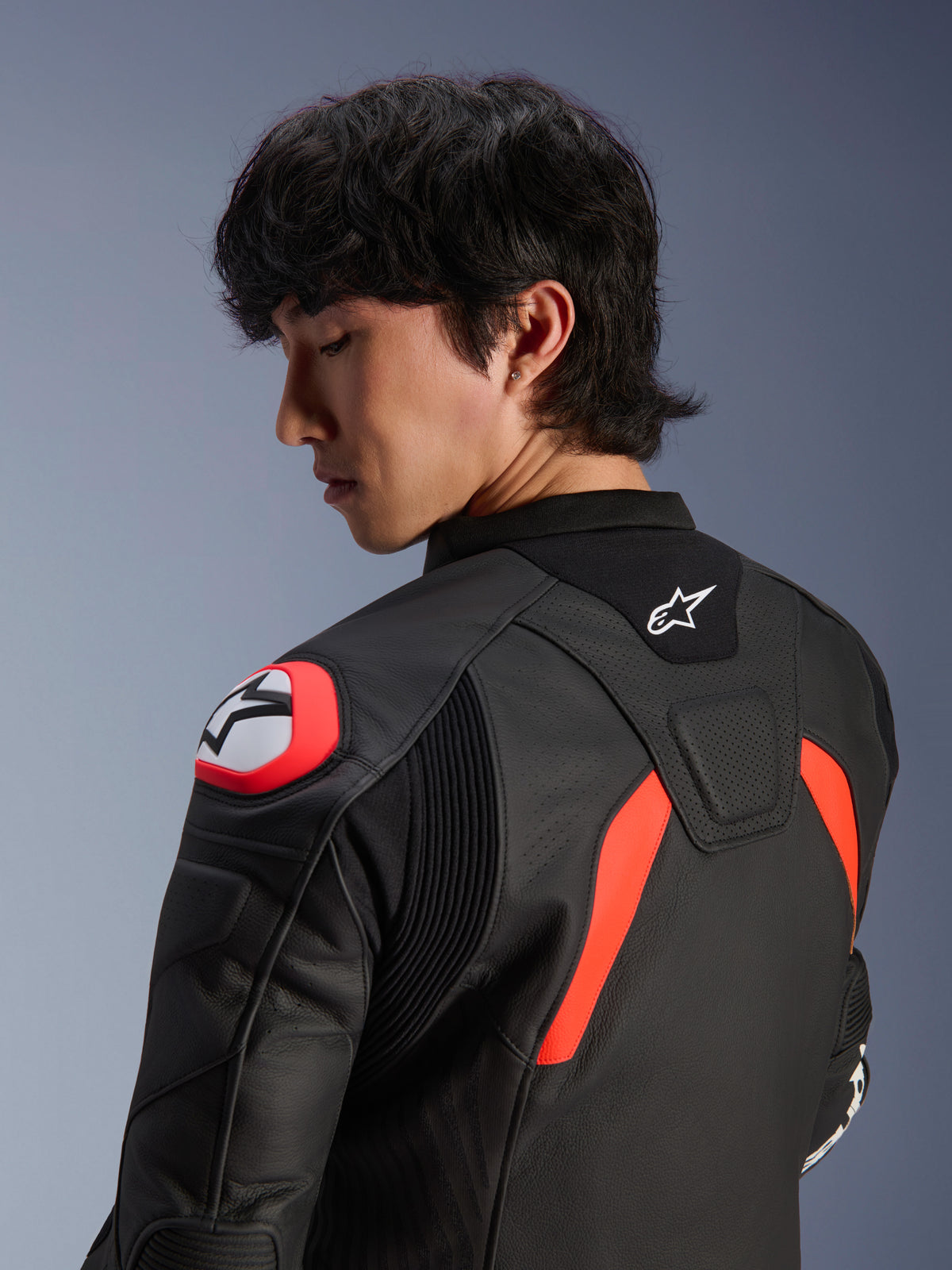Jaqueta de Couro Alpinestars GP Plus R V4 Airflow, preta com detalhes em vermelho fluo e branco, vista aproximada das costas e ombro num modelo, com zonas de couro perfurado, logótipo Alpinestars e proteção de ombro integrada para performance em motociclismo.