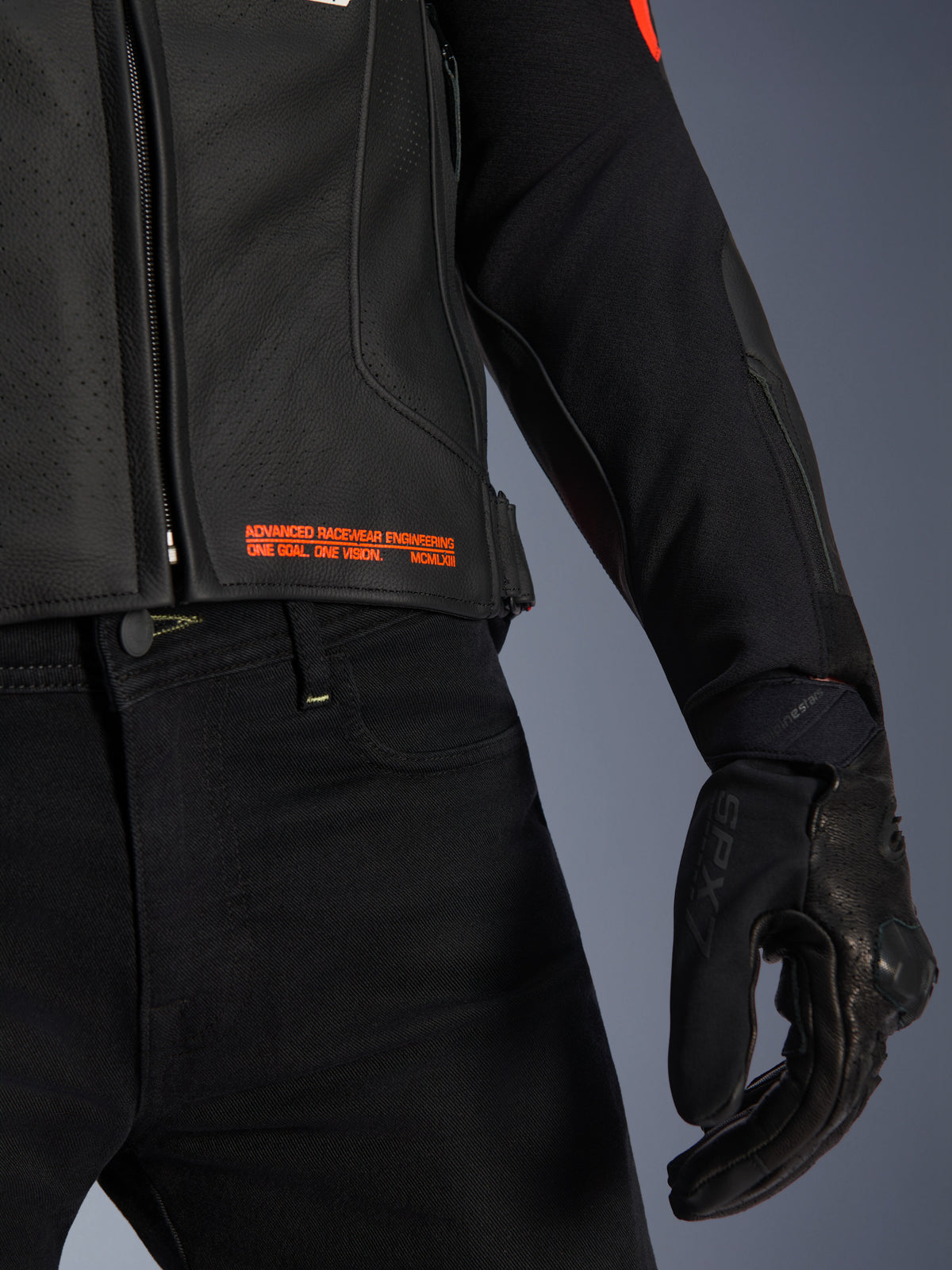 Casaco de couro Alpinestars GP Plus R V4 Airflow, pormenor da cintura e da manga, em couro perfurado preto com texto da marca em vermelho fluo 'Advanced Racewear Engineering', combinado com calças de motociclismo pretas e luva de motociclismo SPX 7