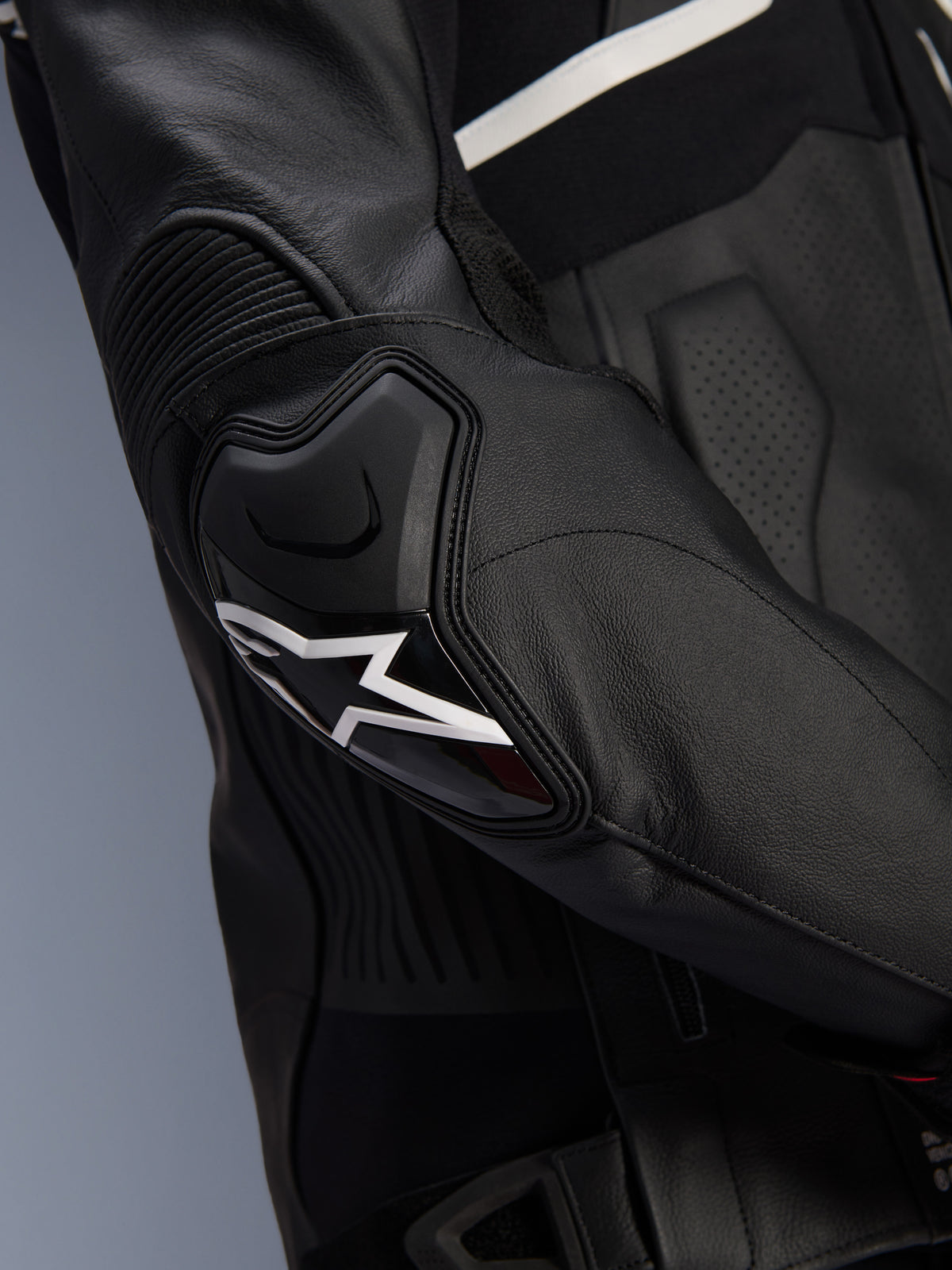 Jaqueta de Couro Alpinestars Atem V5, preto e branco, pormenor do protetor de cotovelo DFS RR com logótipo da estrela branca, apresentando couro em acordeão e texturas perfuradas para condução desportiva