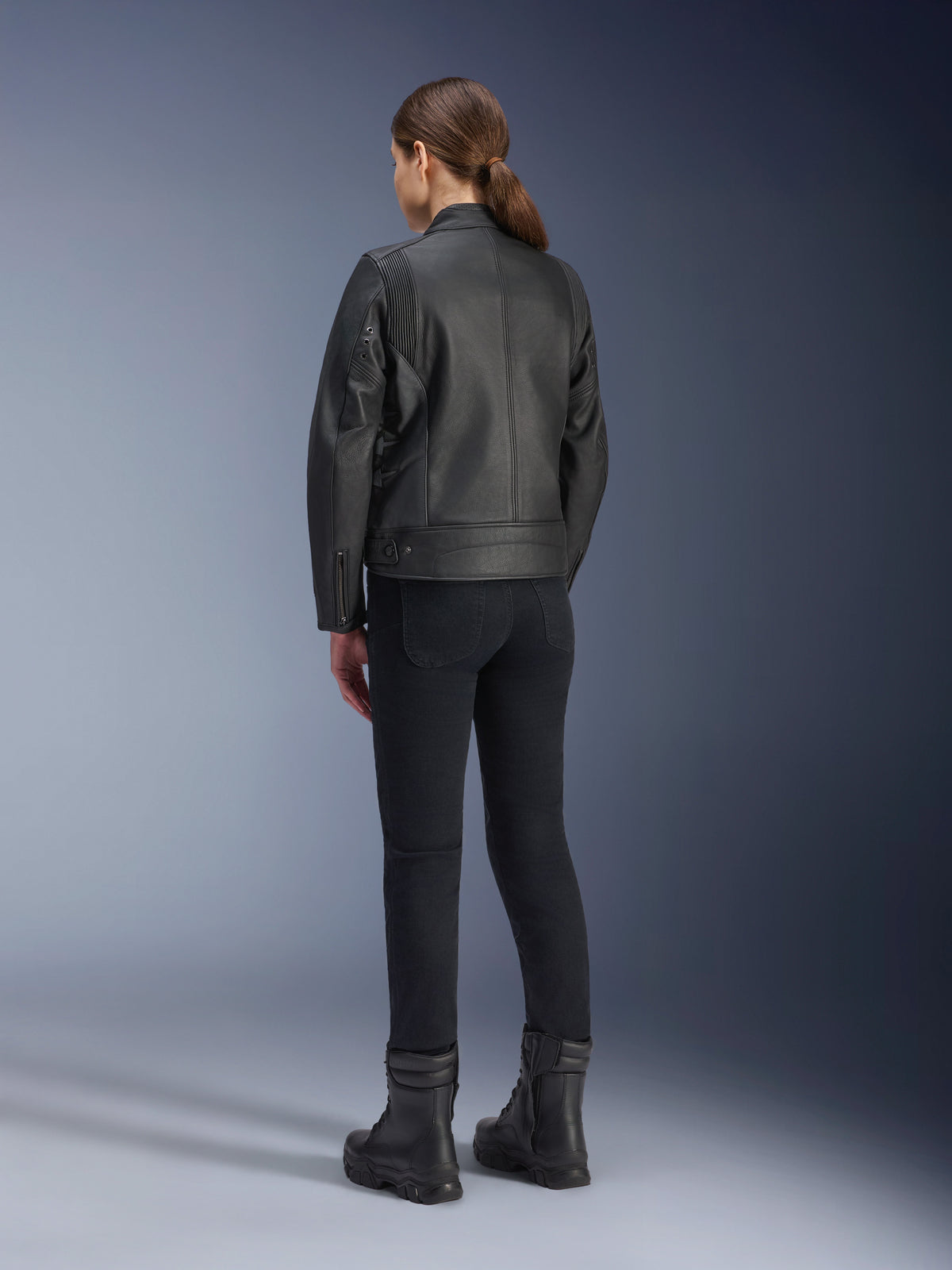 Casaco de Couro Alpinestars Stella Dyno, casaco de motociclismo para mulher, preto, vista traseira mostrando a construção em couro premium e o ajuste personalizado, usado com calças de motociclismo pretas e botas pretas, estilo de condução urbana.
