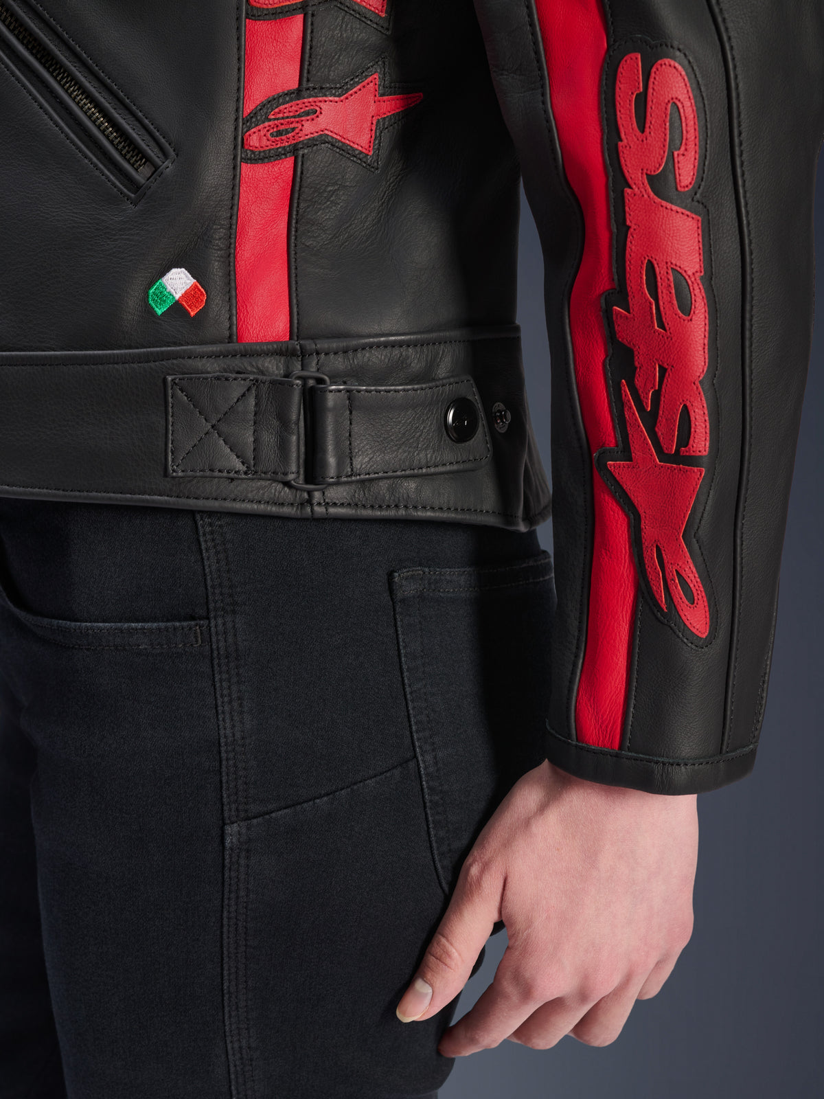 Blusão de Couro Alpinestars Stella Dyno, blusão de motociclismo feminino em couro, Preto Haute Red, vista de detalhe da cintura e da manga, riscas vermelhas com a marca Alpinestars, ajuste de cintura regulável, pequeno bordado da bandeira italiana, construção em couro bovino premium