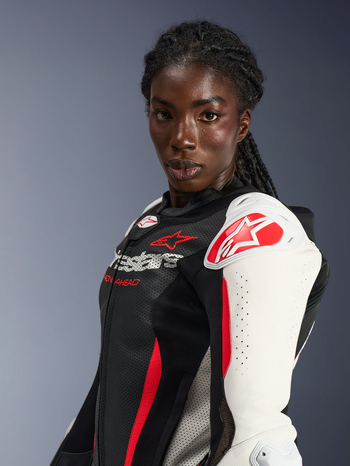 Motociclista feminina a usar o fato de cabedal de 2 peças Alpinestars Stella GP-R7, preto, branco e vermelho fluo, com protetores de ombro brancos com logótipo de estrela vermelha, peito em cabedal perfurado e design inspirado na competição profissional