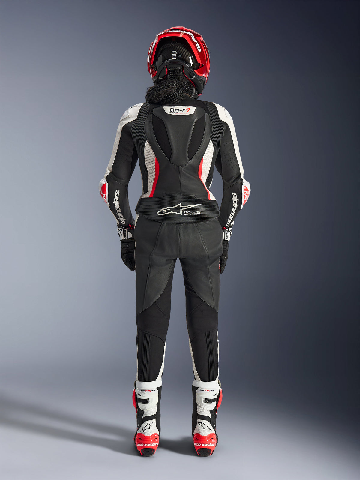 Fato de Cabedal de 2 Peças Stella GP-R7 Feminino, vista traseira, preto, branco e vermelho fluo, com corcova aerodinâmica com marca GP-R7, logótipo Tech-Air Ready na parte inferior das costas, painéis elásticos em acordeão e marca Alpinestars nas mangas, usado com capacete e botas a condizer