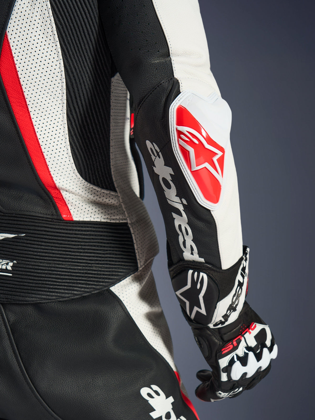 Pormenor do Fato de Cabedal de 2 Peças Alpinestars Stella GP-R7 para Mulher, preto, branco e vermelho fluo, com o slider de cotovelo GP DFS RR com logótipo de estrela vermelha, marca Alpinestars branca no antebraço e painéis detalhados de cabedal perfurado e elásticos em acordeão.