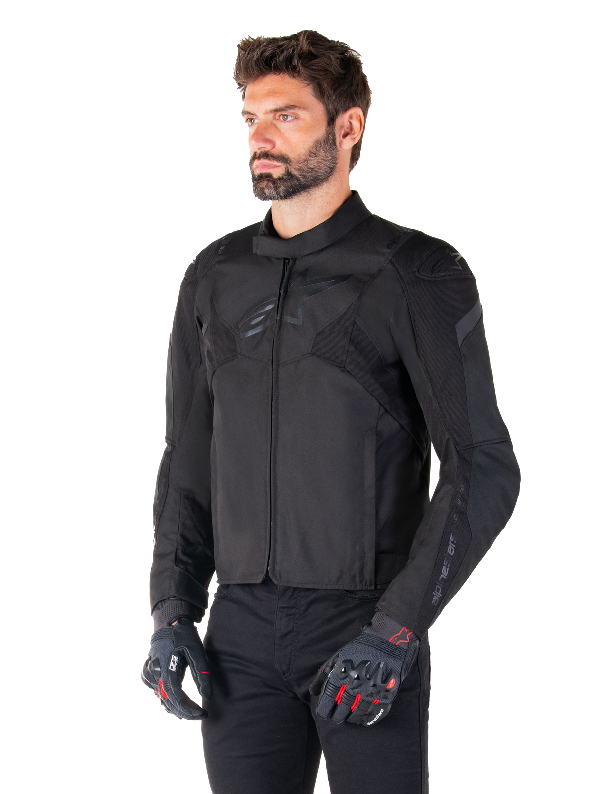 Motociclista a usar o Casaco Impermeável Alpinestars T-Jaws V4 em preto, combinado com calças pretas e luvas de proteção, apresentando um ajuste desportivo elegante, logótipos Alpinestars tonais no peito e ombros e construção têxtil de alta performance