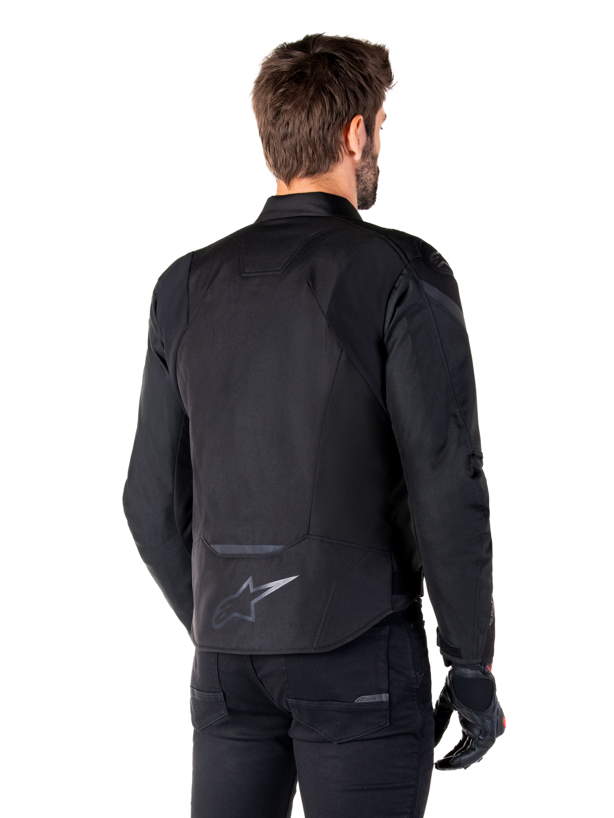 Alpinestars T-Jaws V4 Waterproof Jacket, preto, vista traseira no modelo, com logótipo Alpinestars refletor na parte inferior das costas, parte traseira alongada para maior cobertura, design têxtil desportivo com painéis tonais, usado com luvas de motociclismo pretas