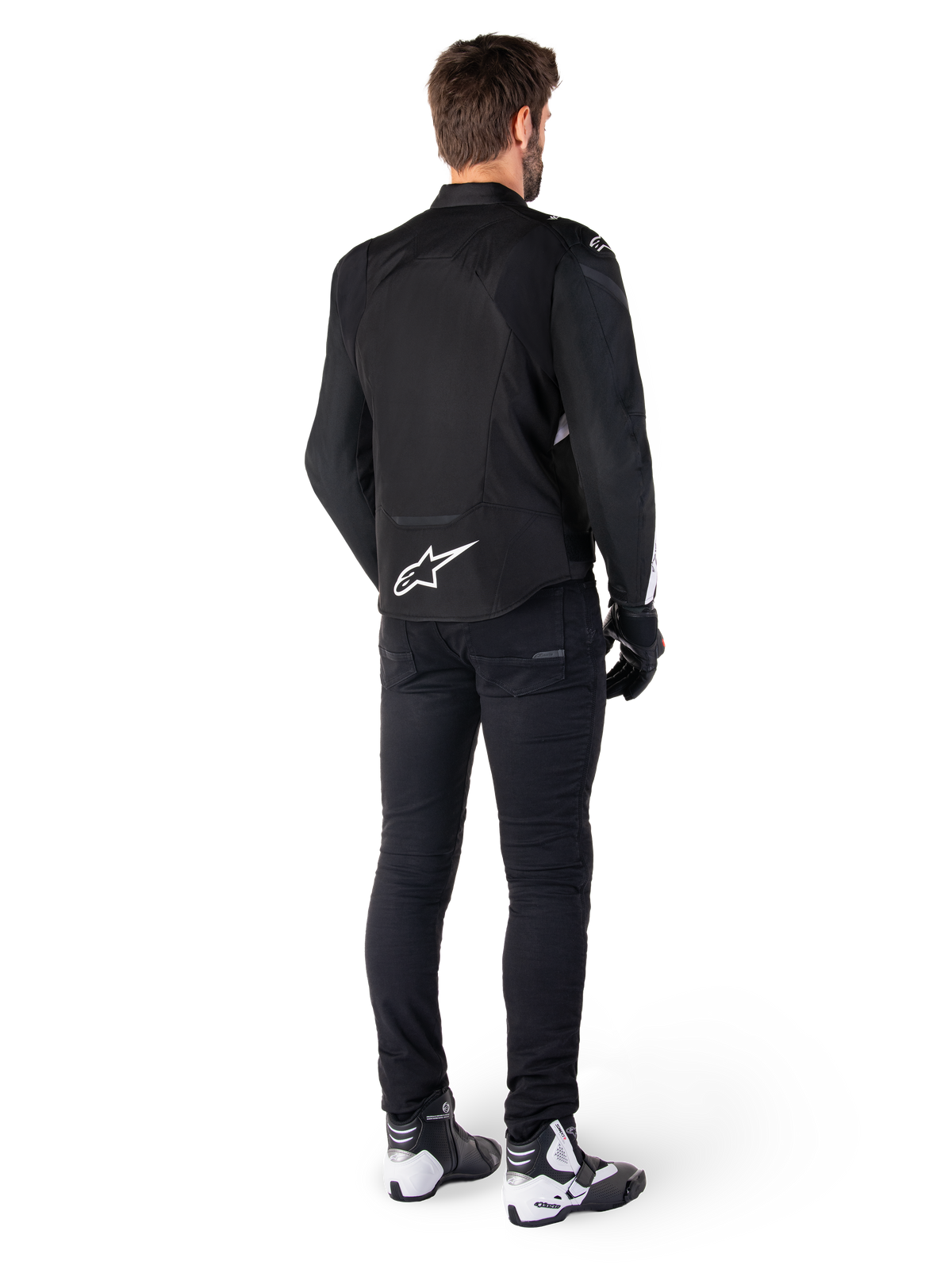 Casaco Impermeável Alpinestars T-Jaws V4, preto e branco, vista traseira com logótipo de estrela branco na parte inferior das costas, usado por modelo com calças de motociclismo pretas, luvas pretas e botas de motociclismo brancas e pretas.