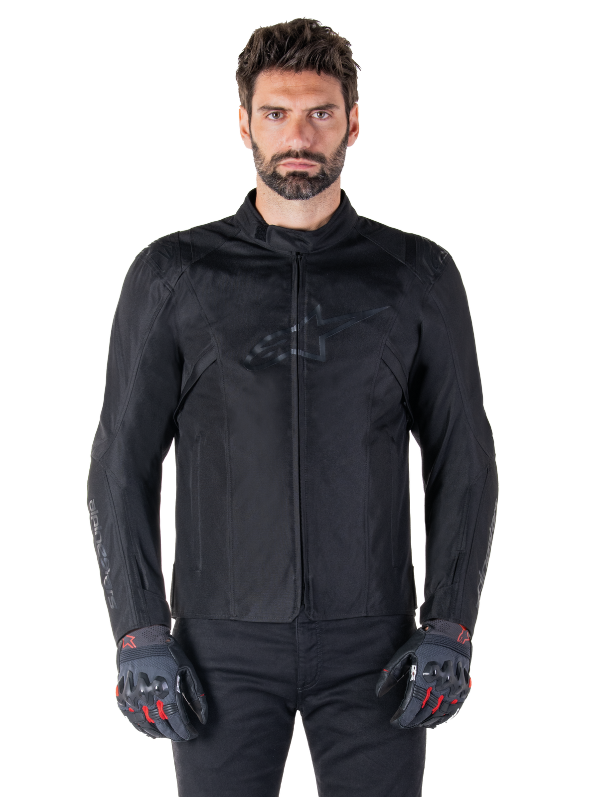 Alpinestars T-SPS V2 Waterproof Jacket, casaco têxtil de motociclismo preto, usado por um condutor com luvas pretas e vermelhas, com gola alta, fecho de correr frontal e logótipo subtil no peito, proteção impermeável para condução desportiva e urbana