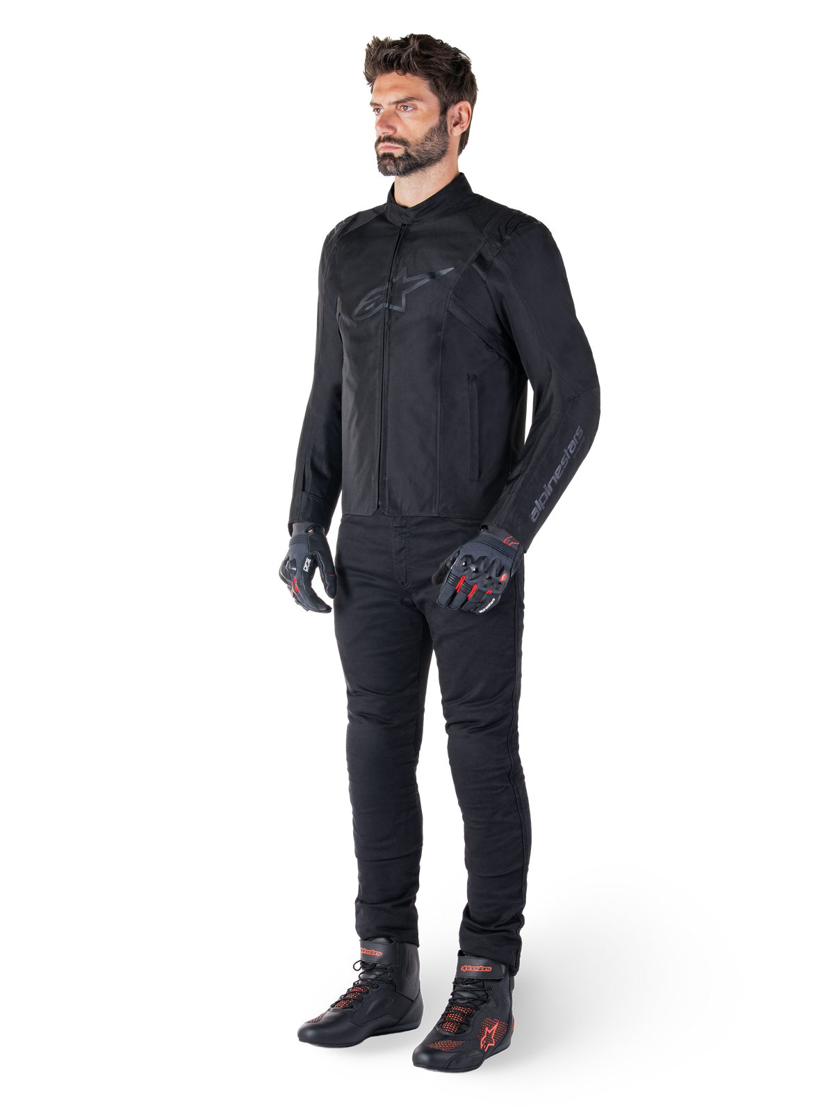 Casaco Alpinestars T-SPS V2 Waterproof, preto, vestido por um modelo masculino com calças pretas a condizer, luvas pretas com detalhes vermelhos e sapatos de condução pretos, equipamento completo de motociclismo para condução urbana e desportiva, fundo branco