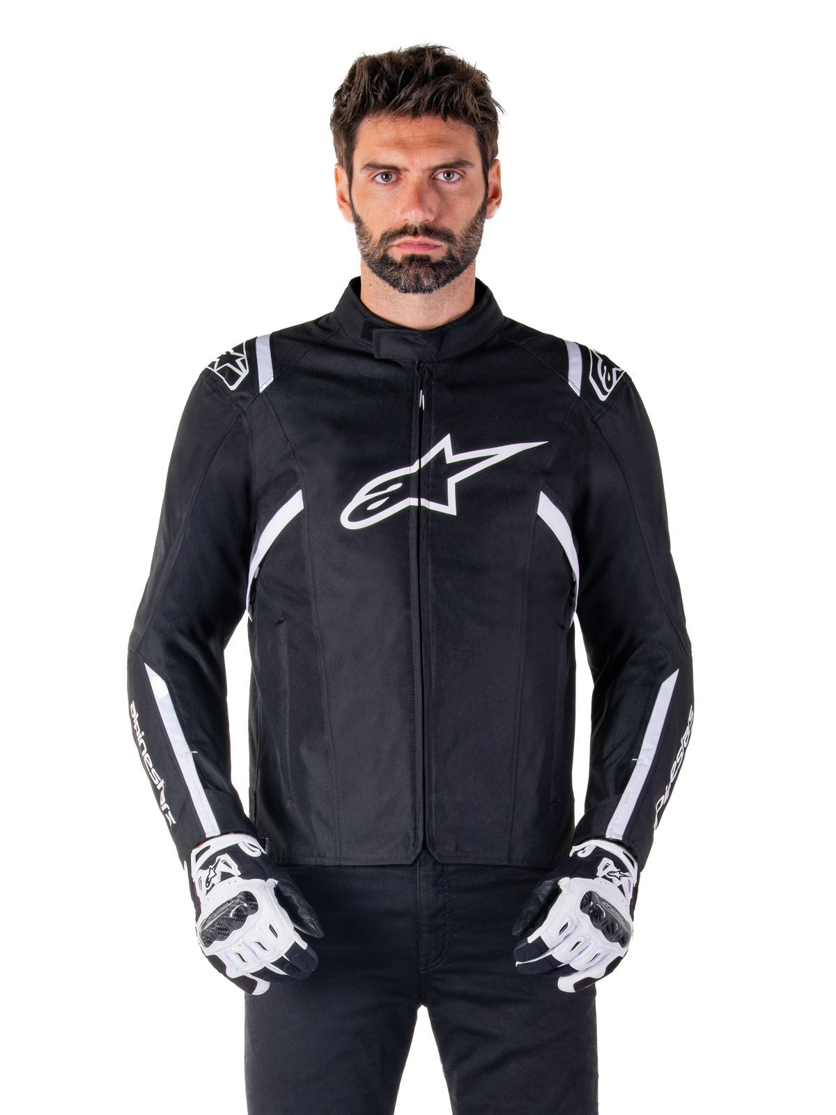 Alpinestars T-SPS V2 Waterproof Jacket, casaco de motociclismo impermeável em tecido preto e branco, vista frontal num modelo, com riscas brancas nos ombros e braços, logótipo Alpinestars grande no peito, usado com luvas de proteção, silhueta elegante de inspiração desportiva