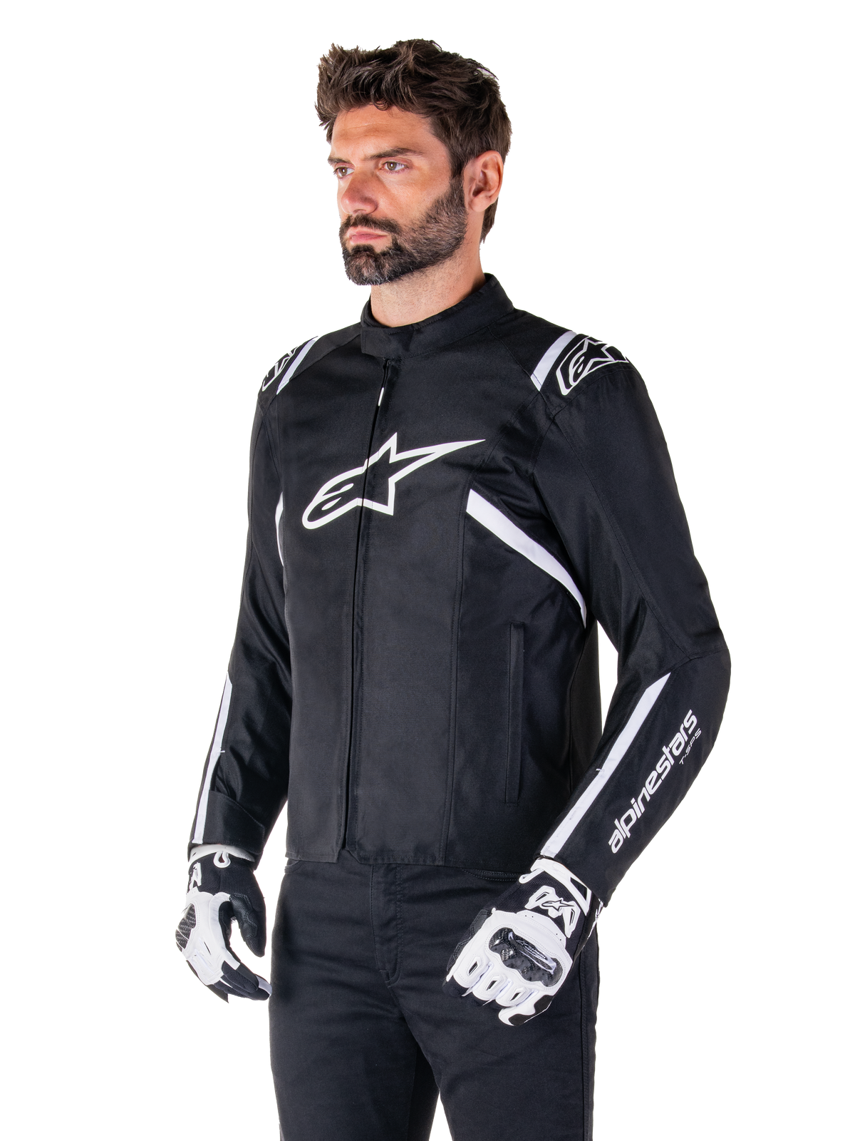 Casaco Alpinestars T-SPS V2 Waterproof, preto e branco, usado por modelo masculino com luvas de motociclismo a condizer, casaco têxtil de corte desportivo com logótipos Alpinestars brancos no peito e nos ombros, marca 'alpinestars T-SPS' na manga, equipamento de motociclismo elegante inspirado na competição
