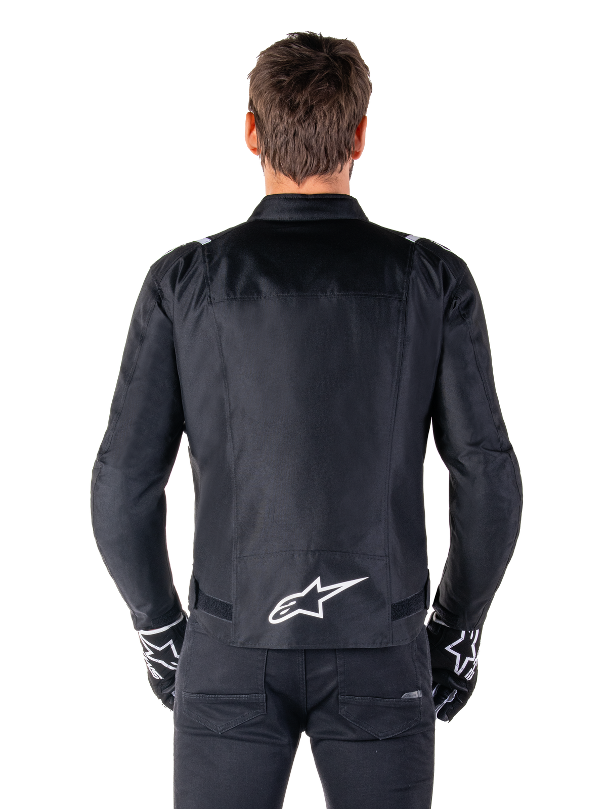 Casaco Alpinestars T-SPS V2 Waterproof, preto e branco, vista traseira mostrando o logótipo branco da Alpinestars na zona lombar, usado com calças e luvas pretas, casaco de motociclismo têxtil de corte desportivo