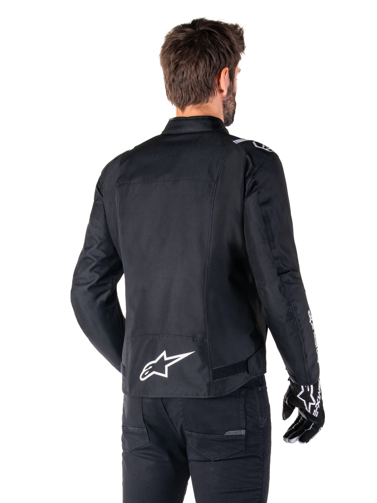 Alpinestars T-SPS V2 Waterproof Jacket, preto e branco, vista traseira de um motociclista masculino a usar o casaco, logótipo Alpinestars branco na parte inferior das costas, construção têxtil com corte desportivo, usado com calças e luvas de condução pretas