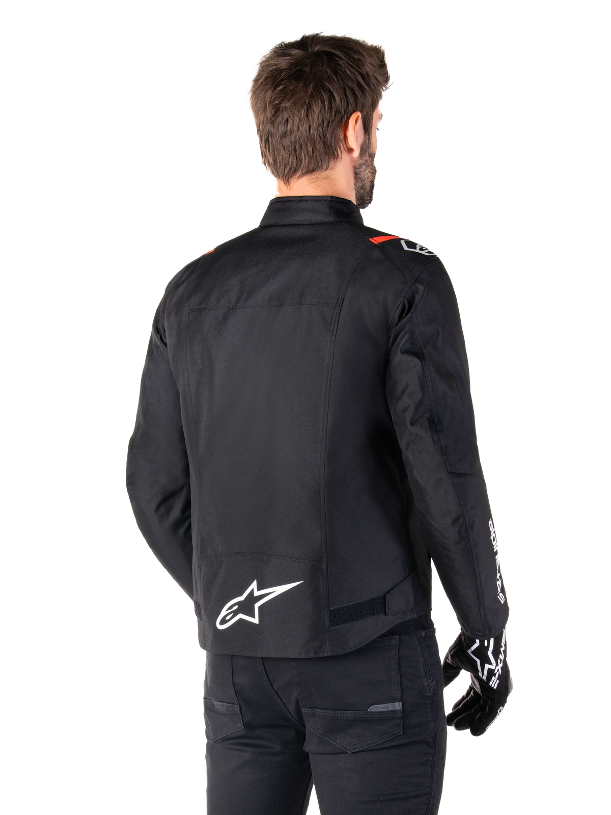 Casaco Impermeável Alpinestars T-SPS V2, preto, branco e vermelho fluo, vista traseira, com logótipo Alpinestars branco na zona inferior das costas e detalhes vermelhos nos ombros, usado com luvas e calças de motociclismo pretas, casaco de motociclismo têxtil de estilo desportivo