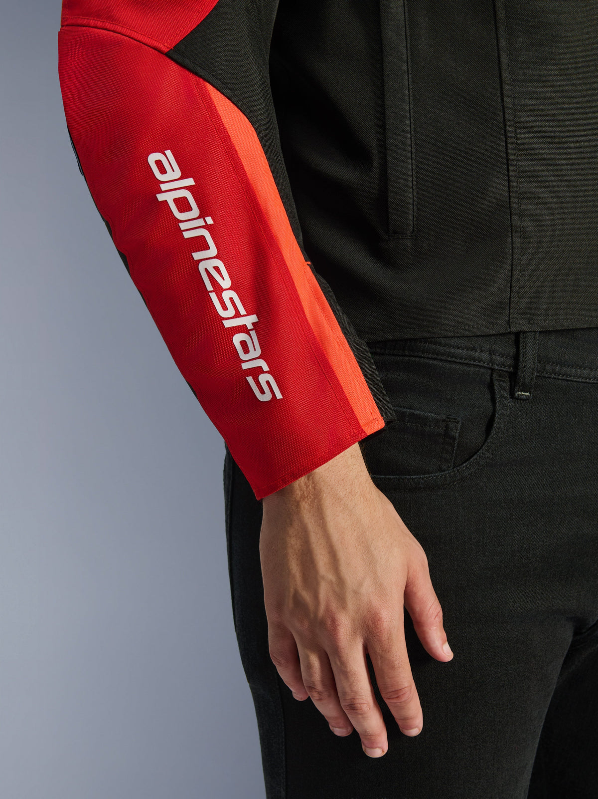 Casaco Impermeável Alpinestars T-SPS V2, casaco de motociclismo, preto e vermelho, pormenor da manga com logótipo da marca branco na vertical num painel vermelho, construção têxtil durável com design de inspiração desportiva